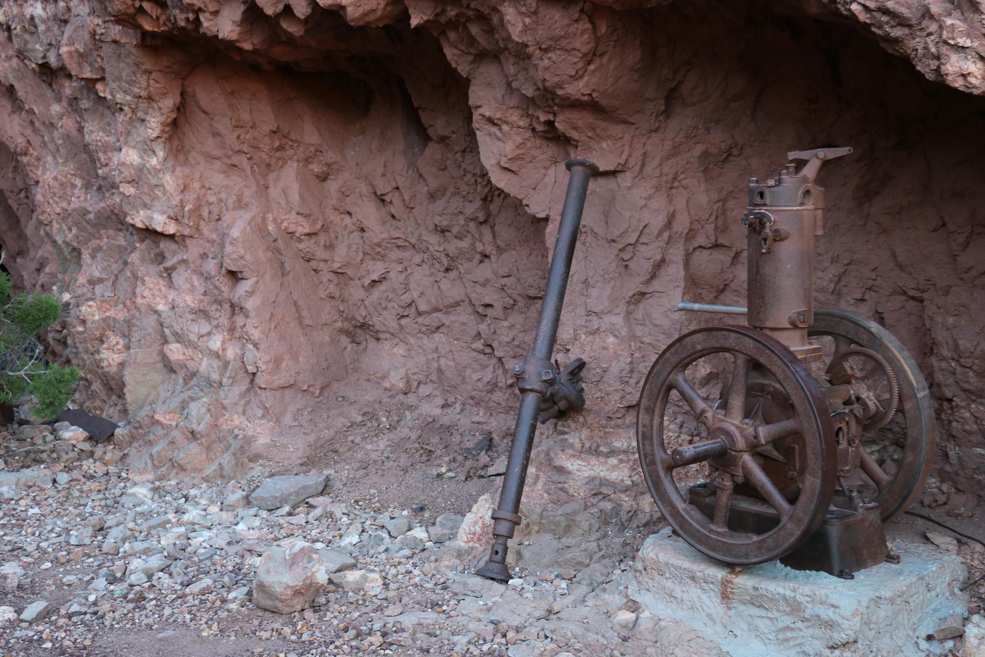 Old rusty mining equipment sits under a rocky overhang in dim light.