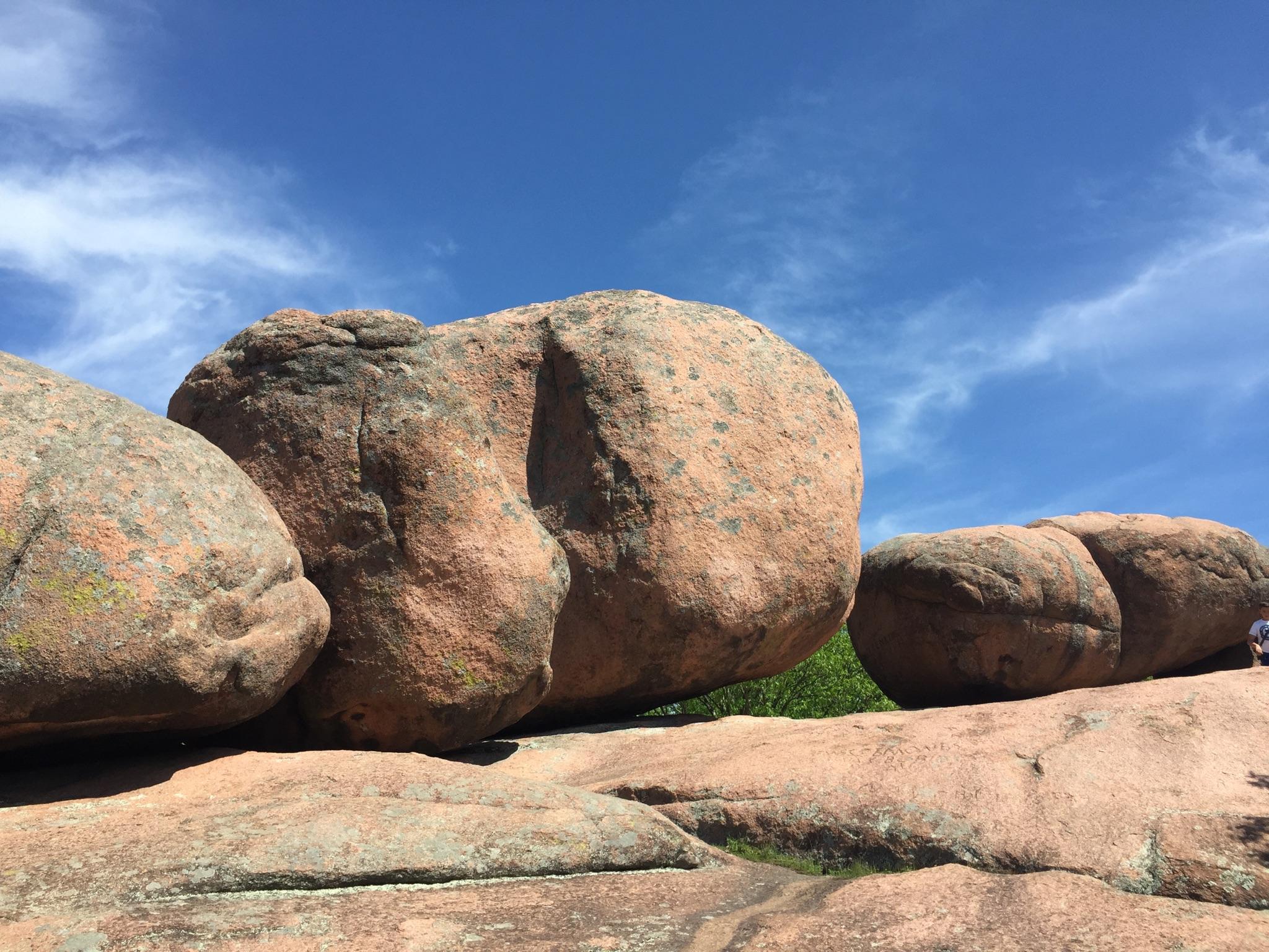 Massive reddish-brown boulders under a bright blue sky with wispy clouds.