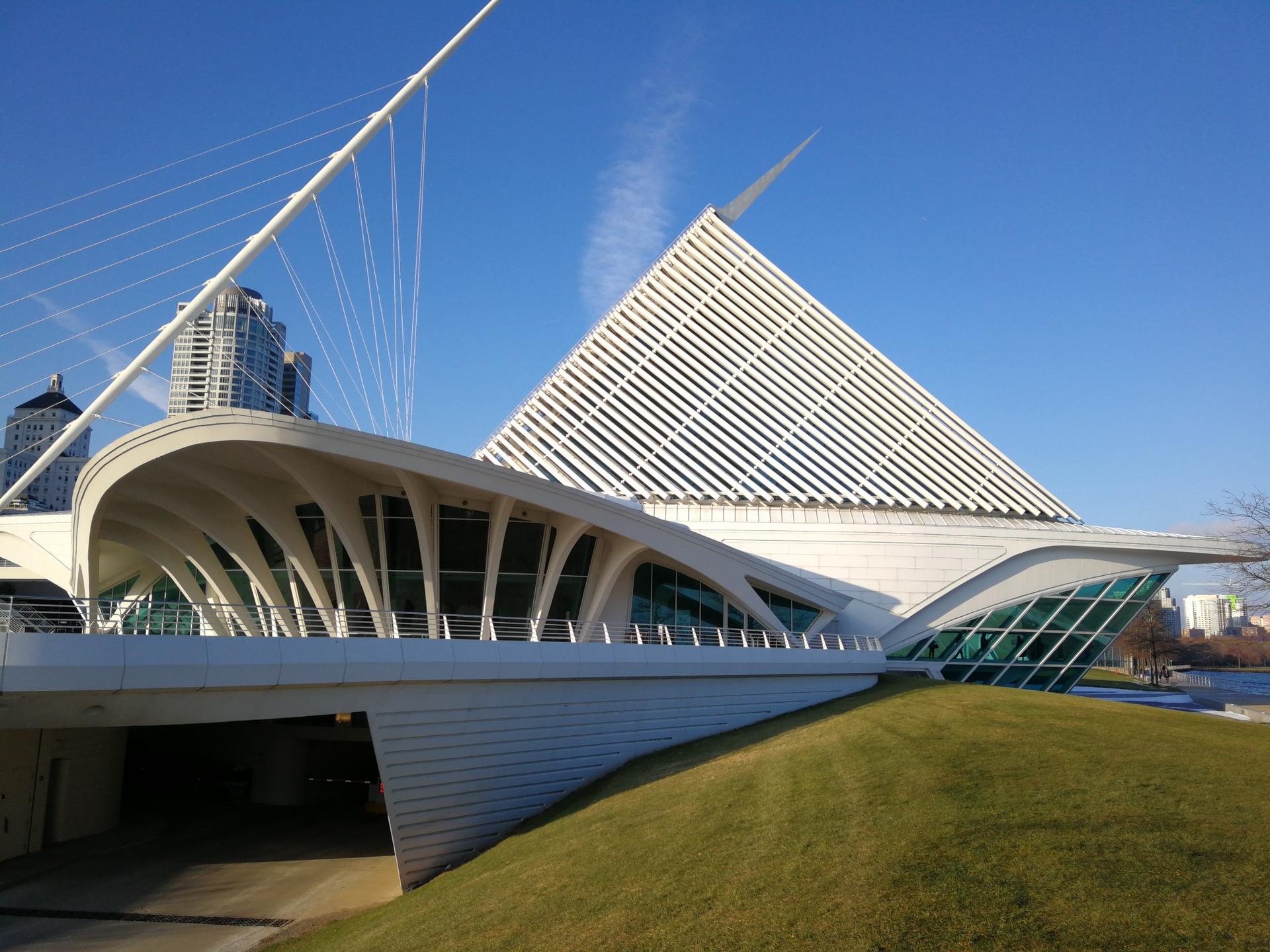 Modern white building with unique architecture, grassy hill, and blue sky.