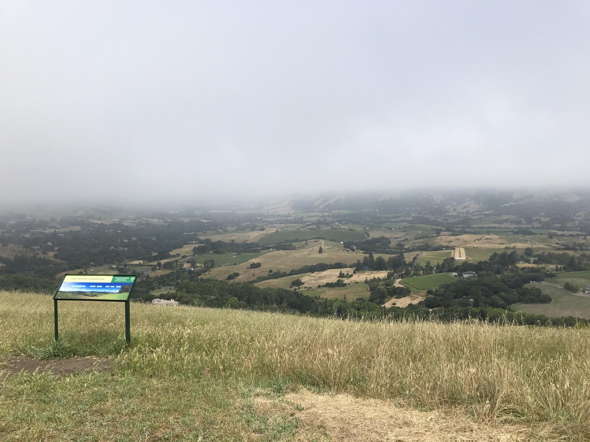 An information sign overlooks a vast, hazy valley under a cloudy sky.