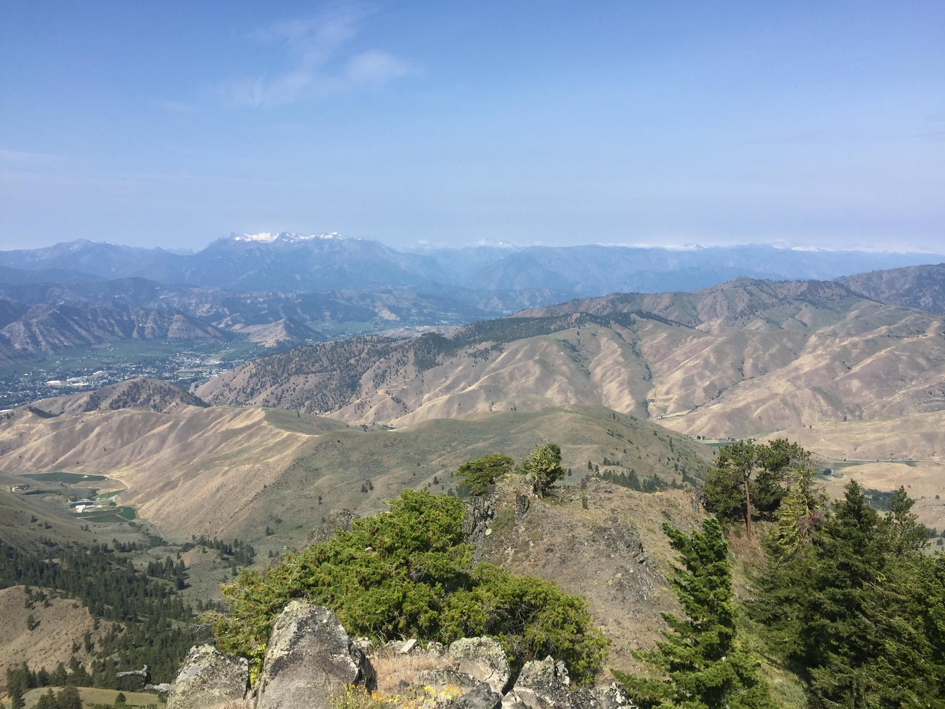 Vast mountain landscape with rolling hills and distant snow-capped peaks under clear sky.