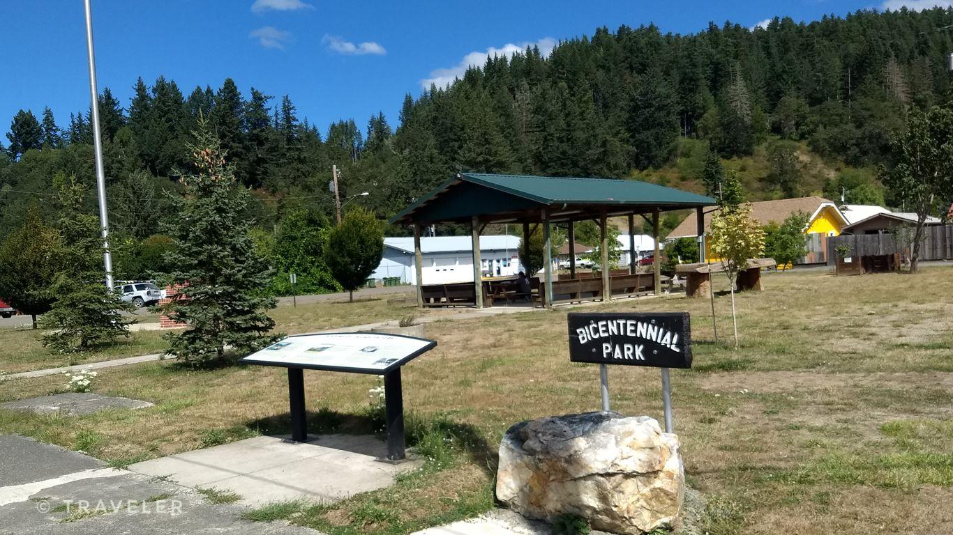 Sunny park with a covered pavilion, green grass, and forested hills.