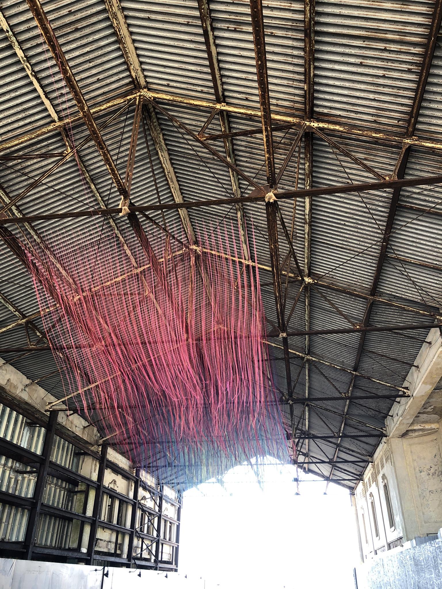 Industrial building interior with a corrugated metal roof and red hanging art.
