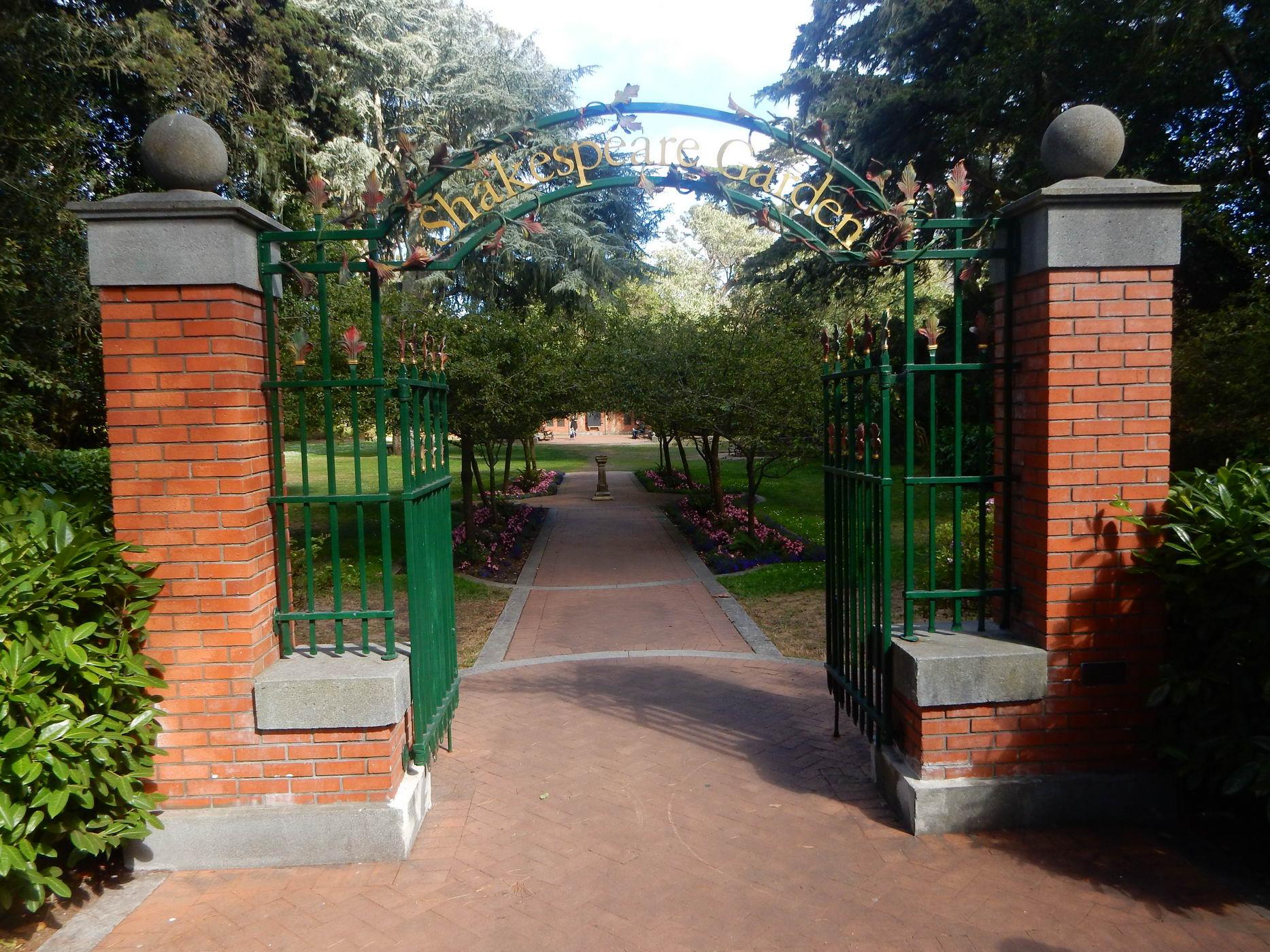 Ornate green gate with brick pillars opening to a garden path.