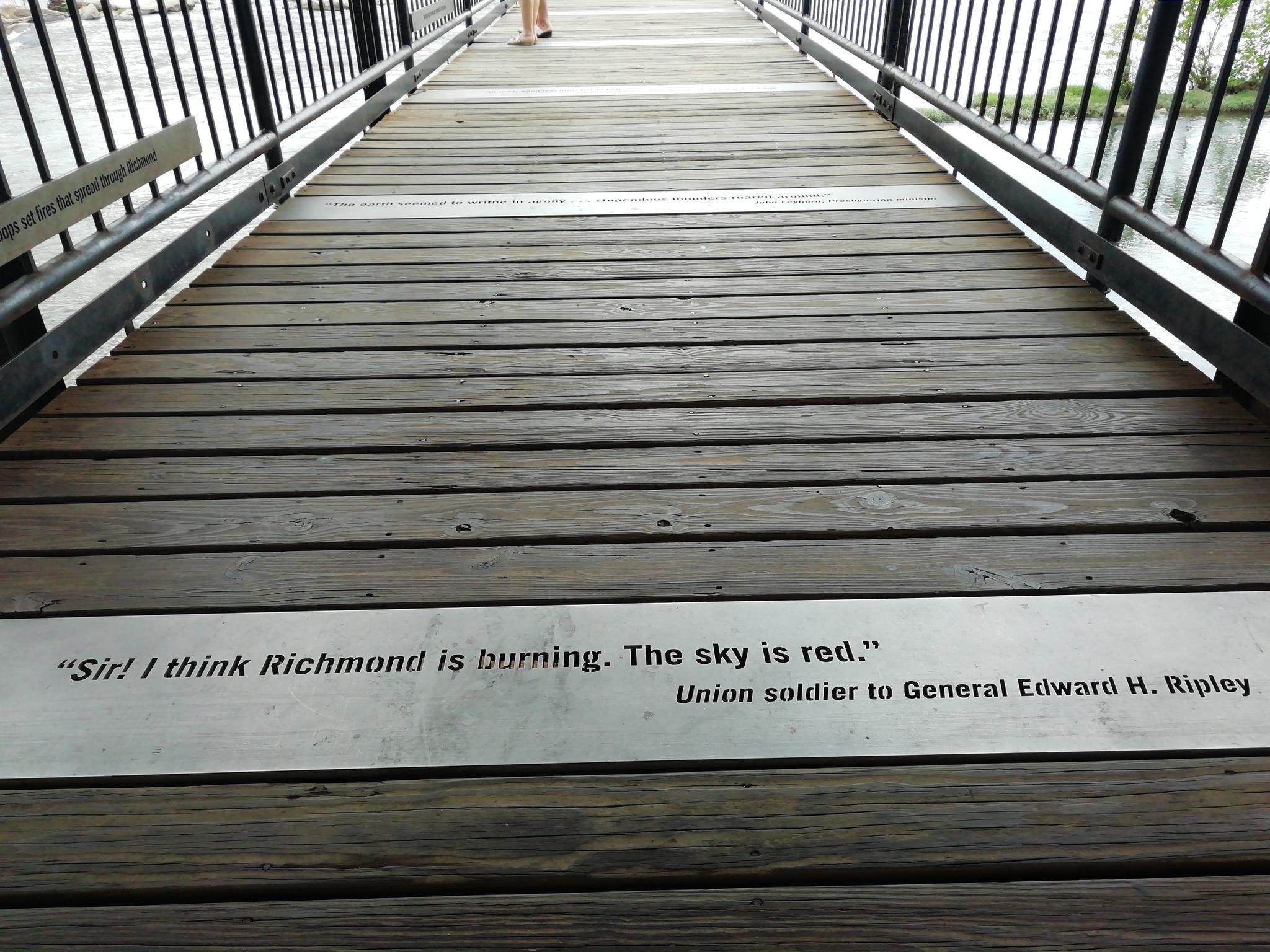 Wooden boardwalk with a historical quote embedded, leading towards a person.