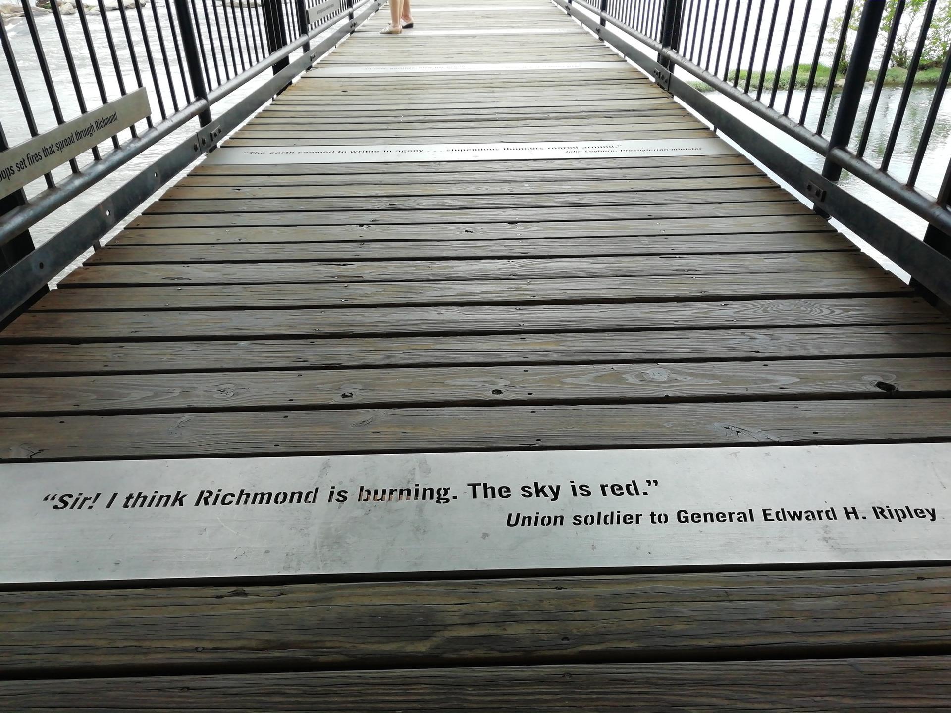 Wooden boardwalk with a historical quote embedded, leading towards a person.
