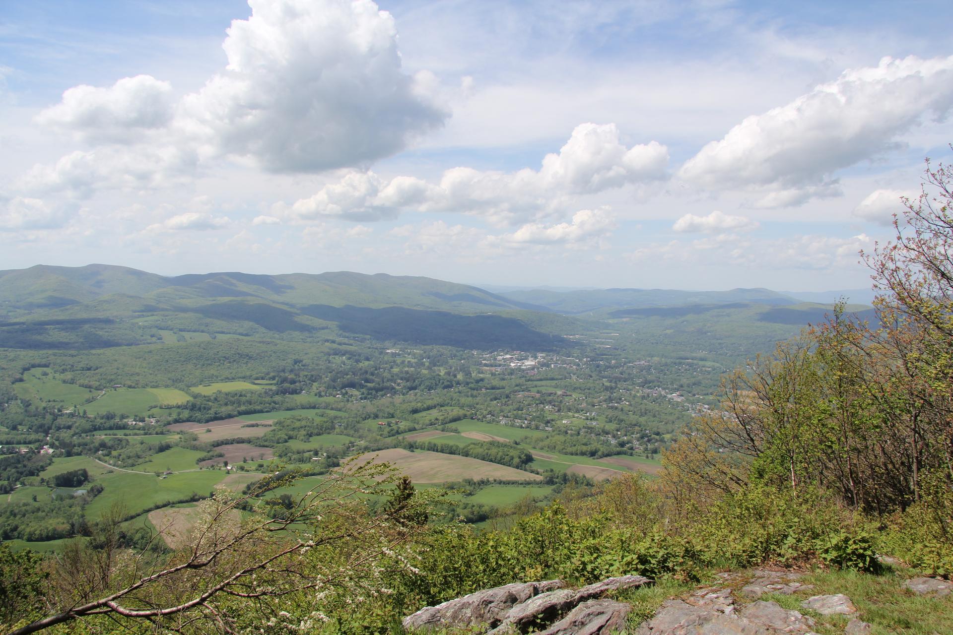 Expansive green valley and distant town under a bright, cloudy sky.