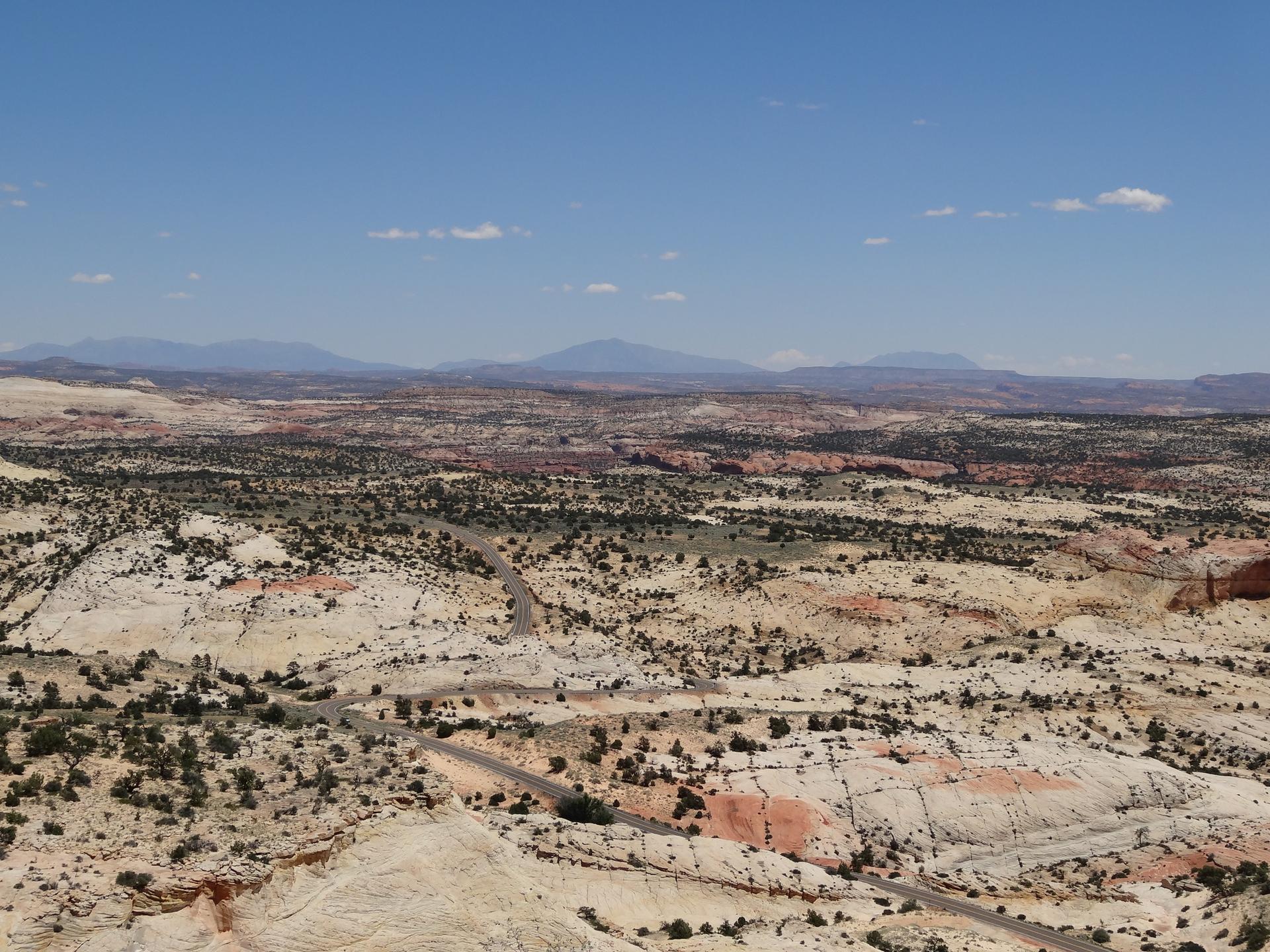 Expansive desert vista with a winding road through light-colored and red rock.