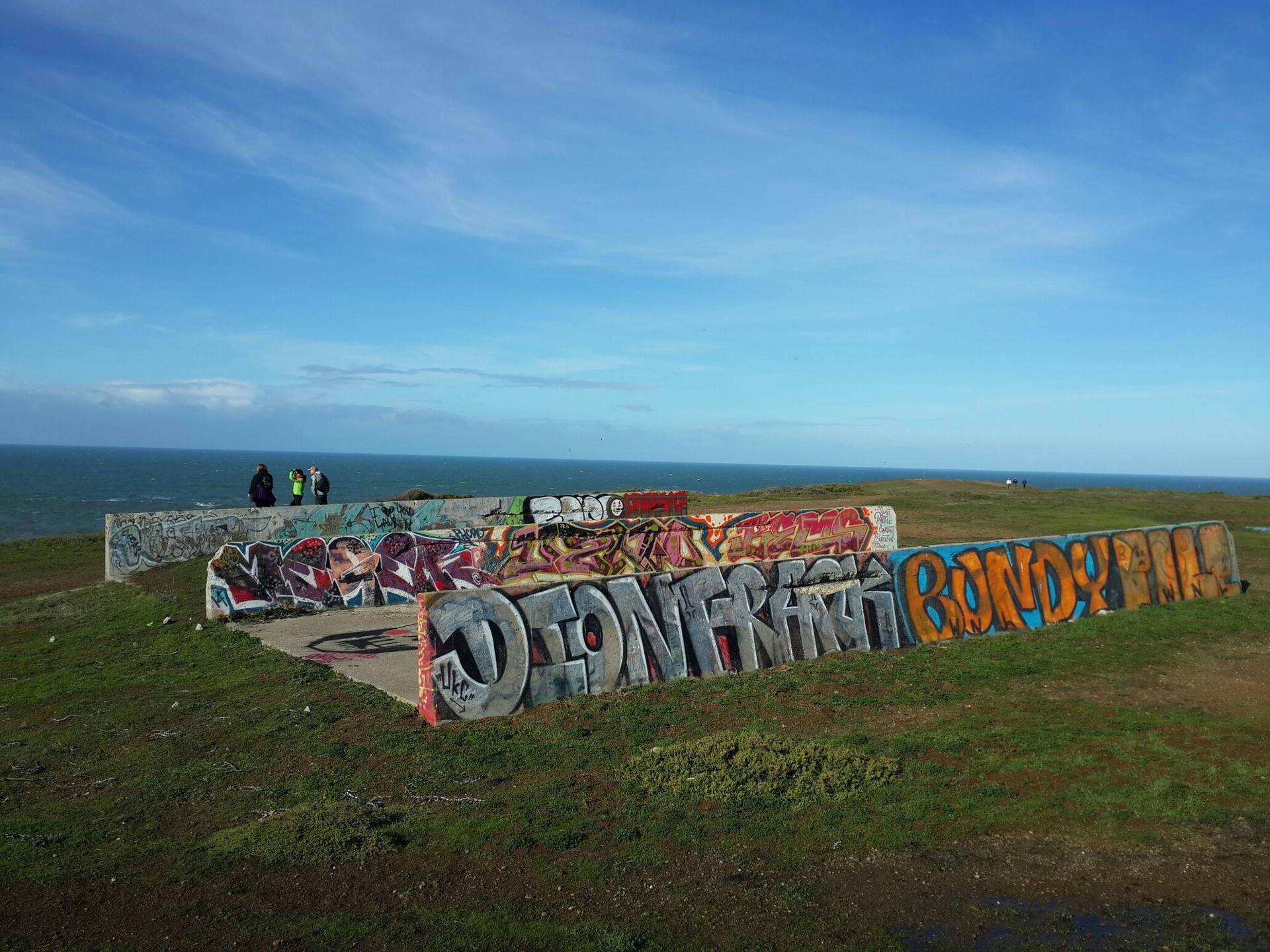 Graffiti-covered concrete walls on a grassy clifftop overlooking the ocean.