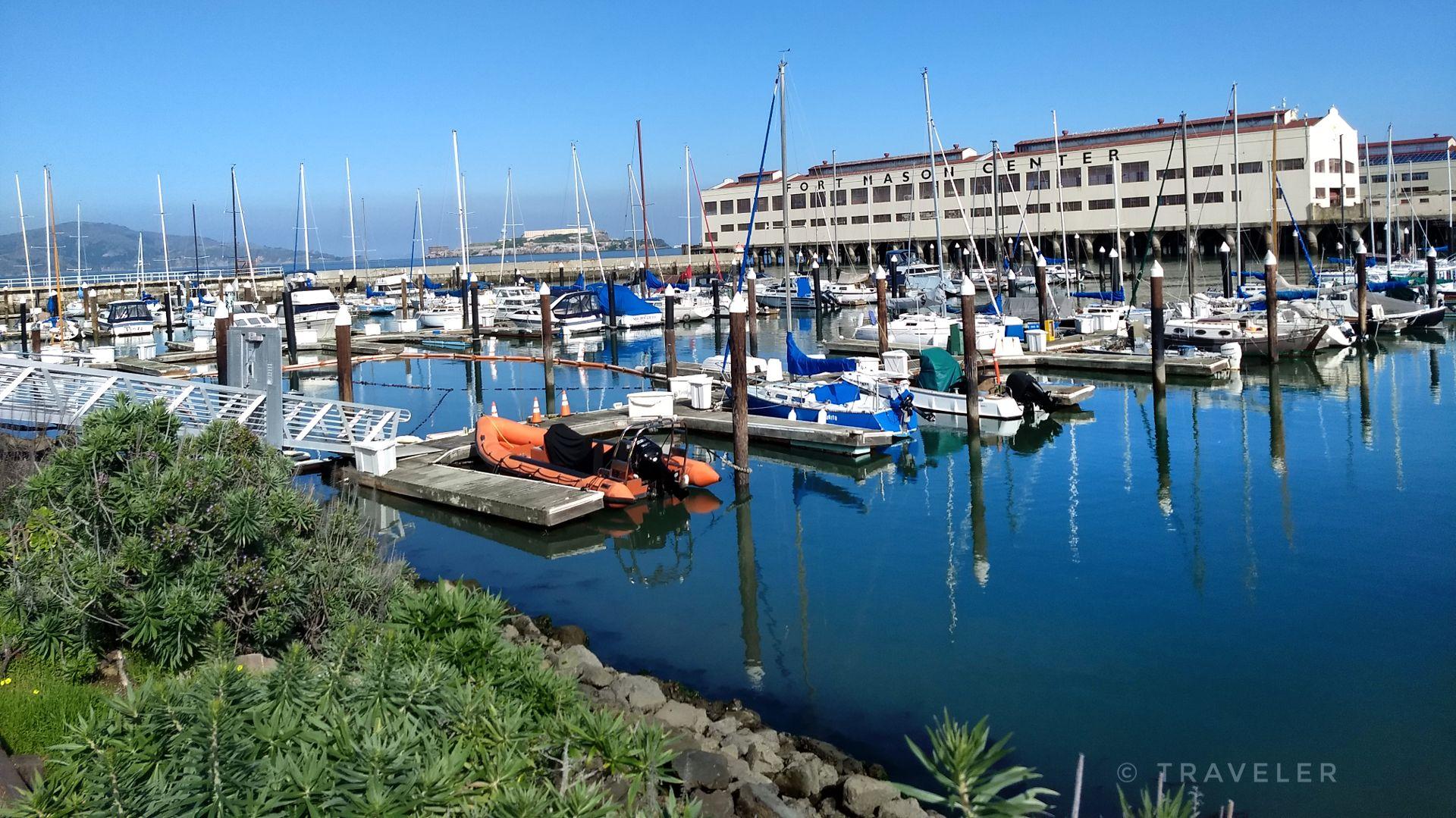 Bright sunny day at a marina with many boats and a large waterfront building.