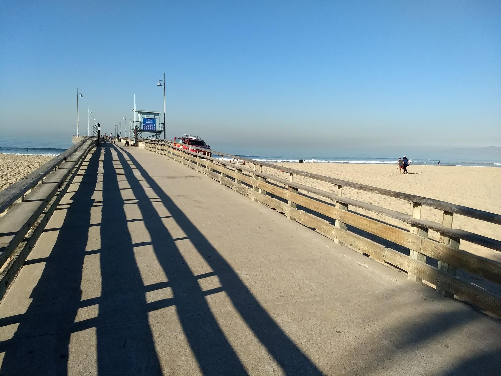 Long pier extending onto a sunny beach with distant people.
