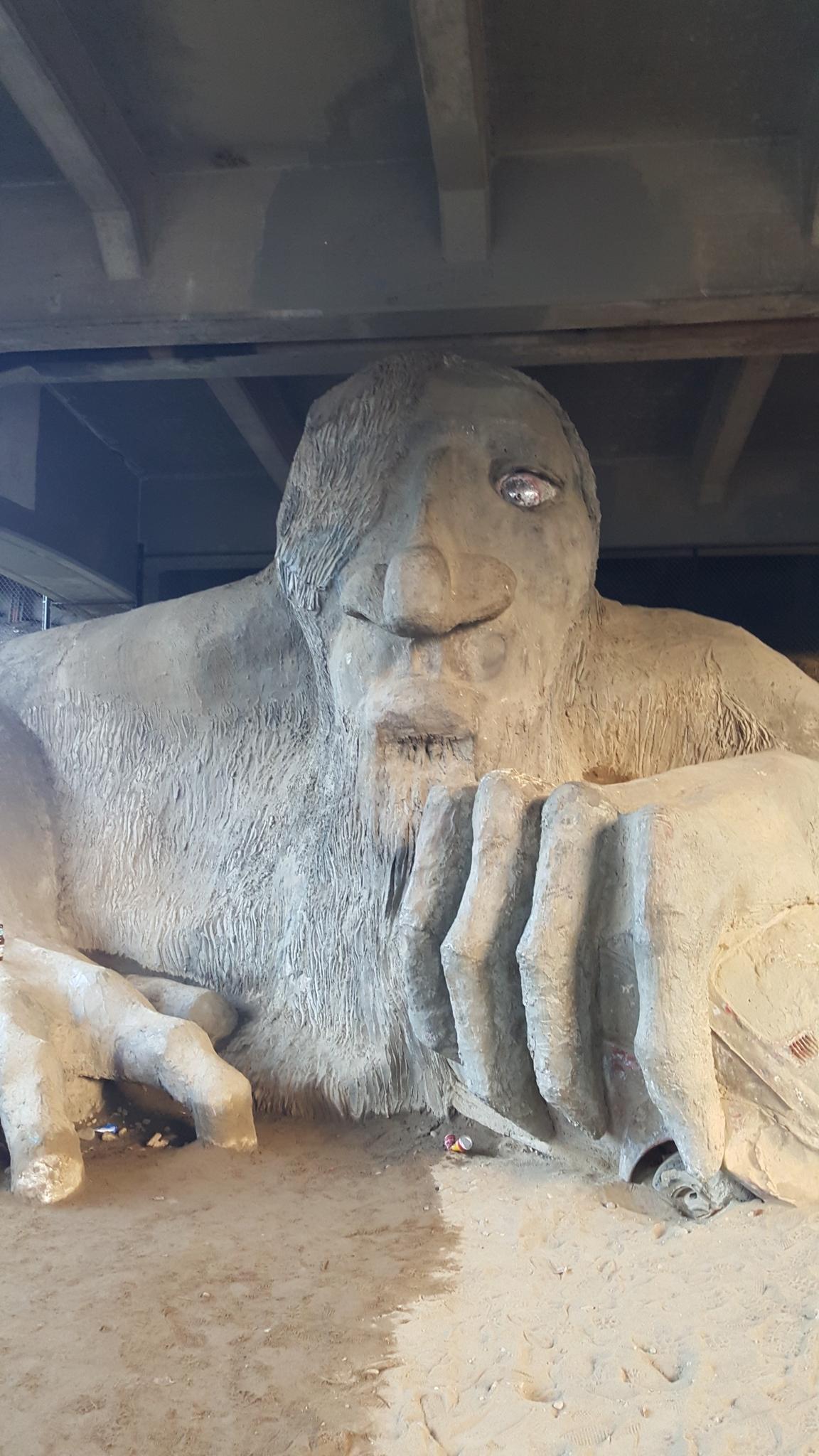Large concrete sculpture of a troll-like figure under a dark overhang.