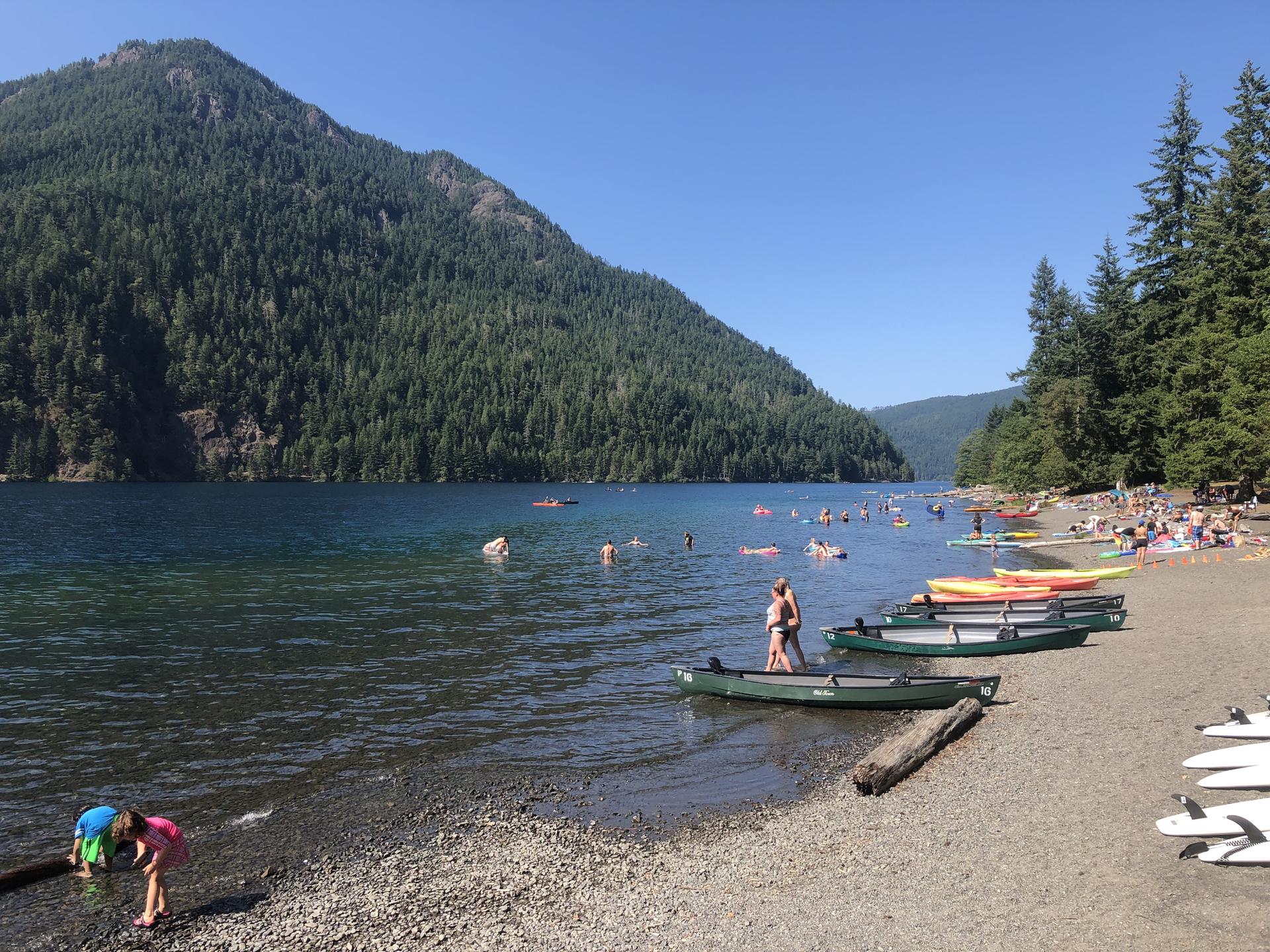 Sunny day at a lake with people swimming, paddling, and relaxing on the shore.