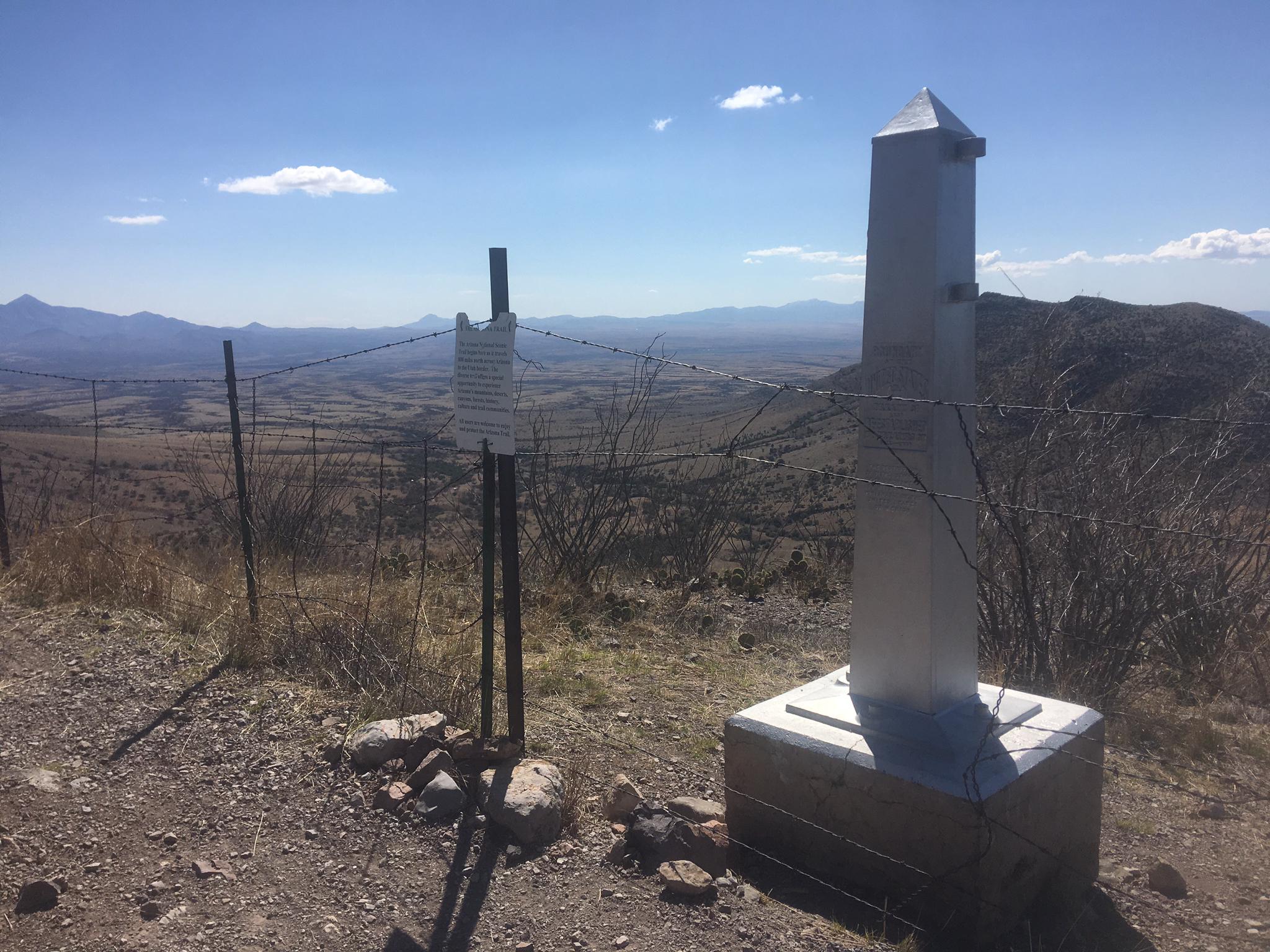 Metal monument and fence on a hilltop overlooking a vast, dry landscape.