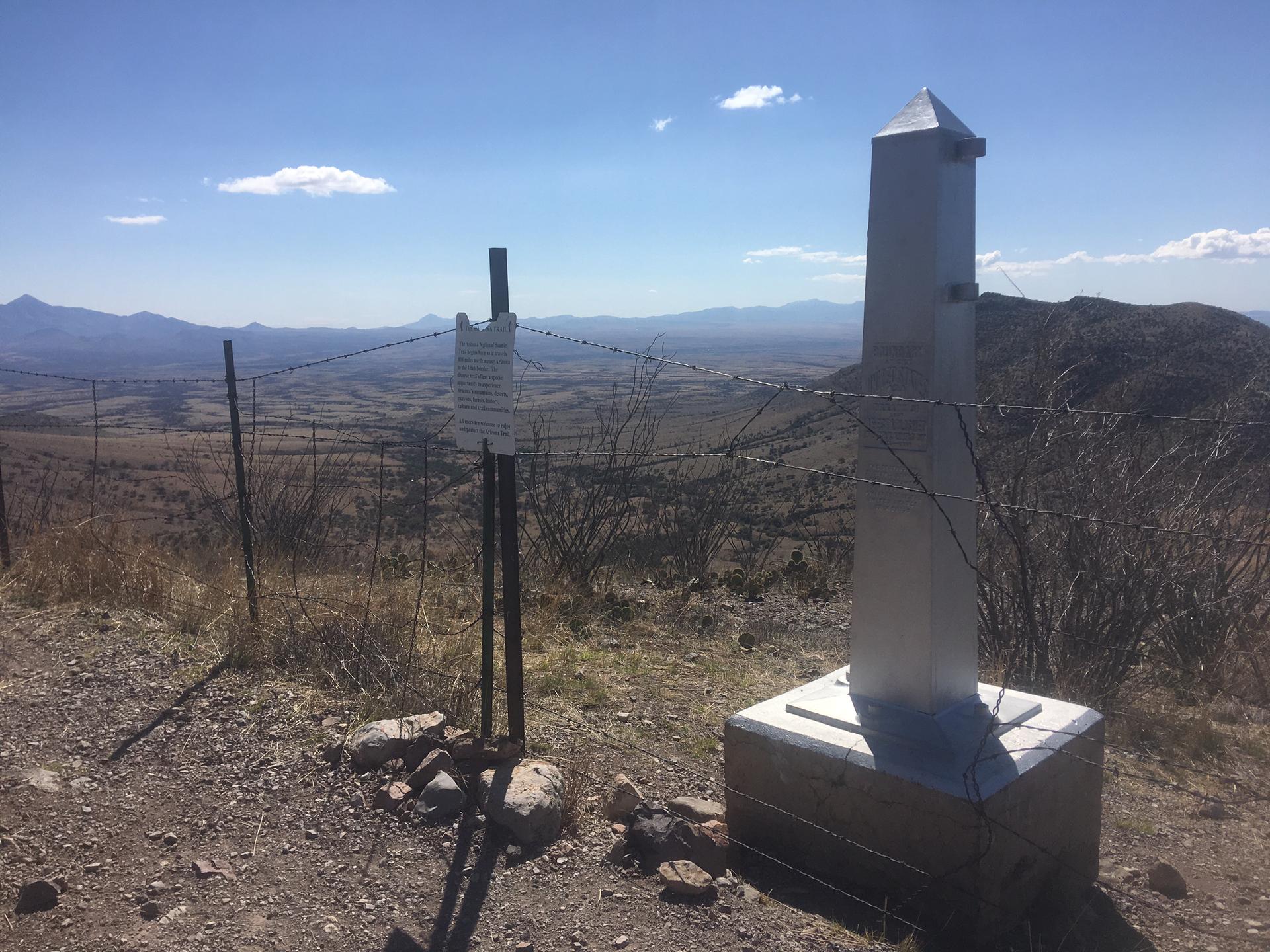 Metal monument and fence on a hilltop overlooking a vast, dry landscape.