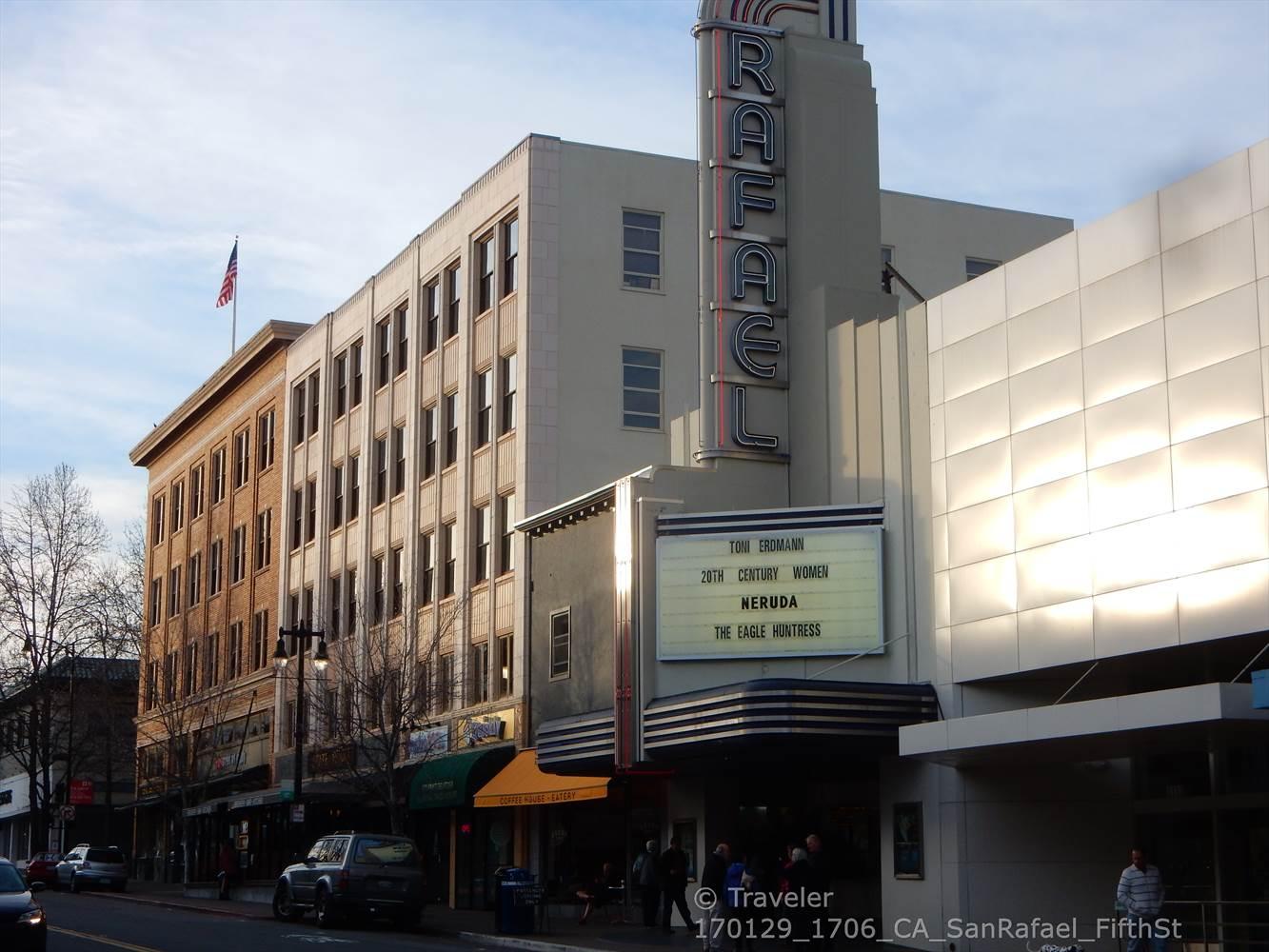 Art deco building with a tall sign on a busy street with people.
