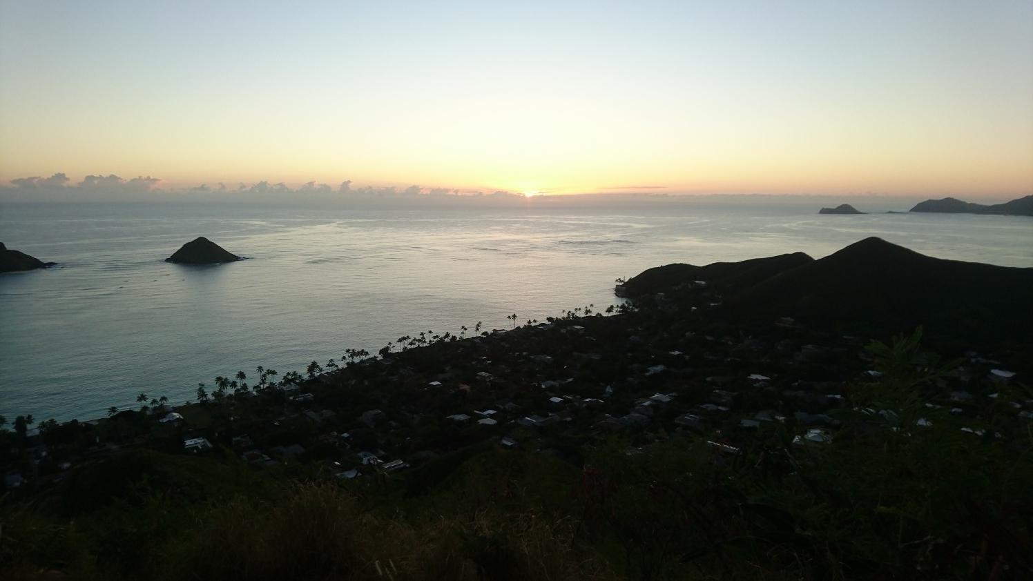 Sunset over the ocean with islands and a coastal town in silhouette.