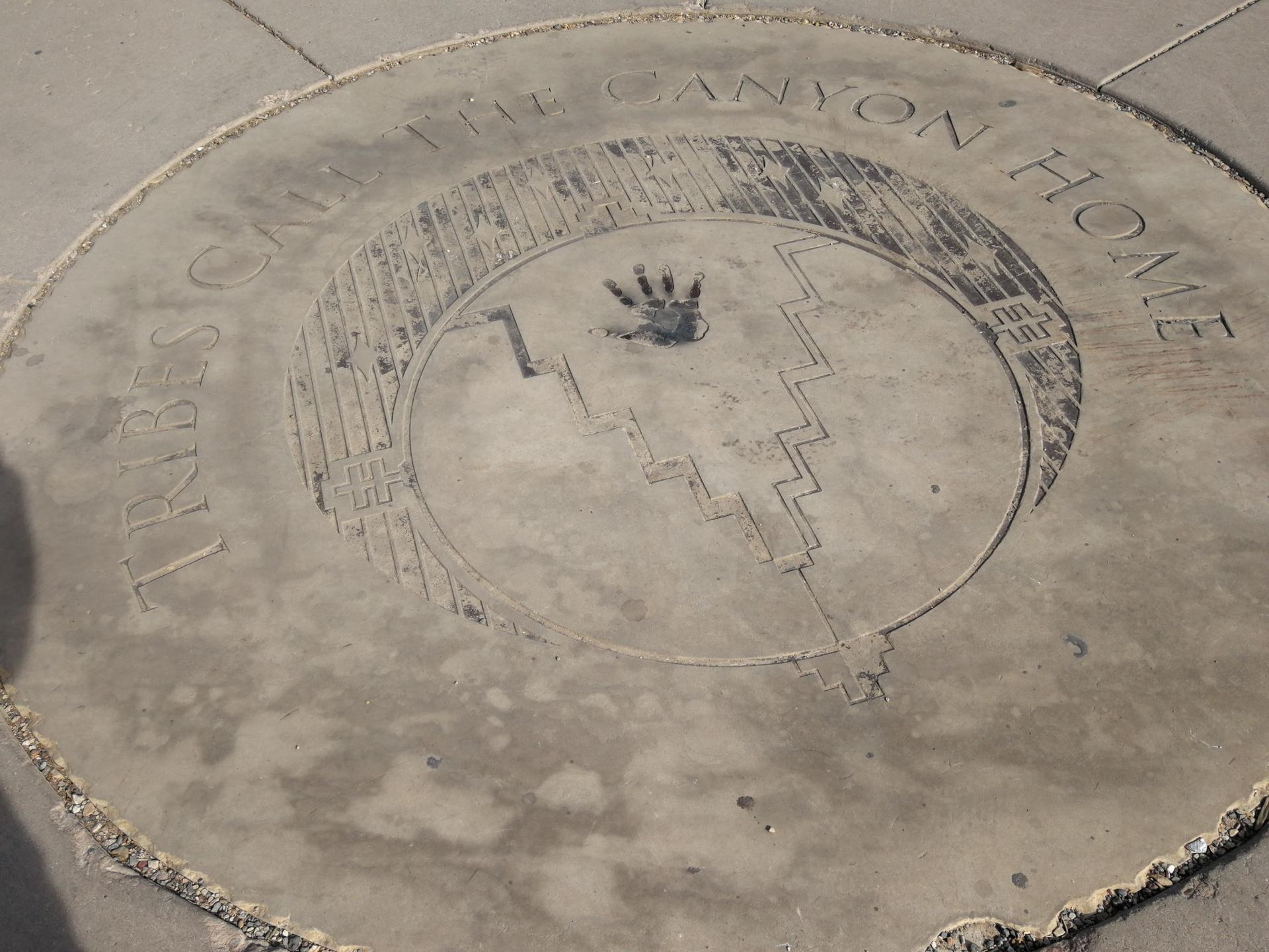 Circular concrete marker on ground with a handprint and text.