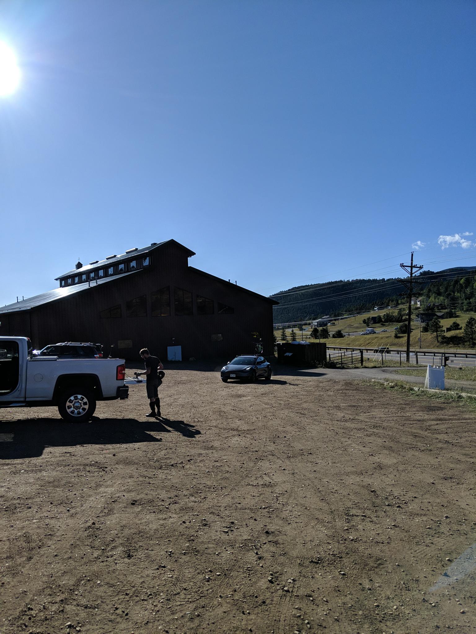 A person stands near a white truck in a sunny dirt lot.