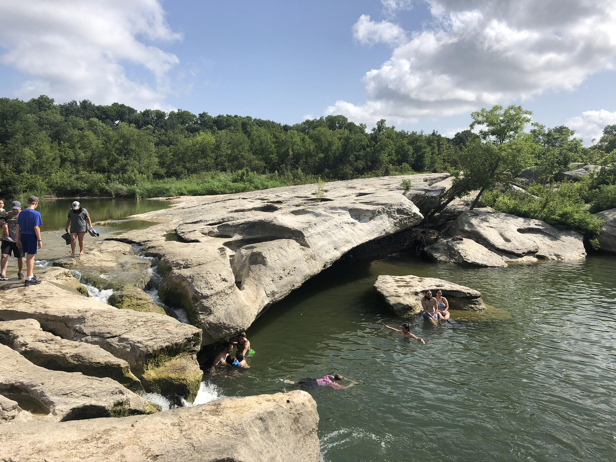 People swimming and standing on large rocks in a wide river.
