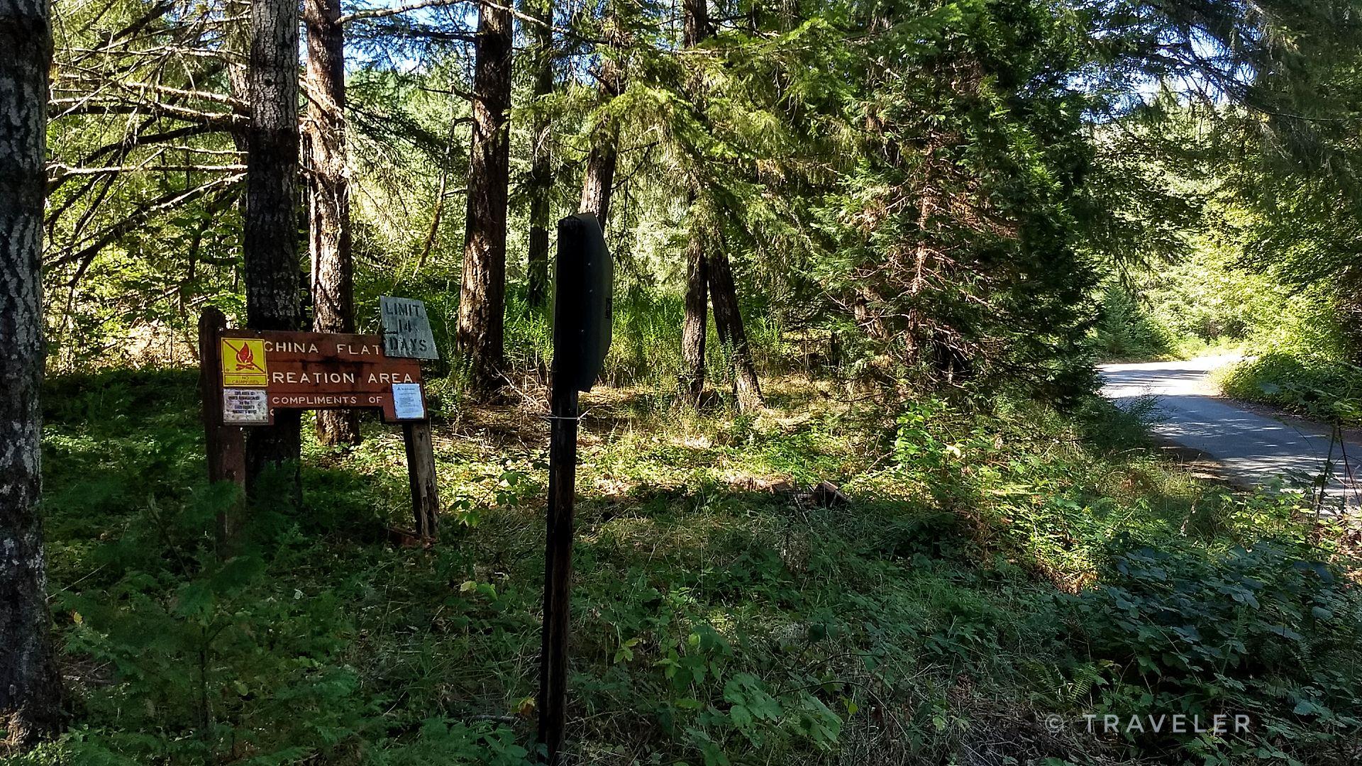 Wooden sign in a sunlit forest clearing next to a dirt path.