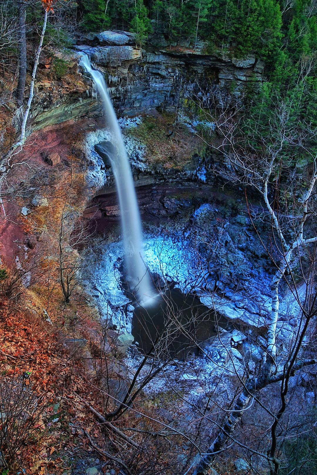A waterfall plunges into a pool, surrounded by colorful, illuminated rocks and trees.