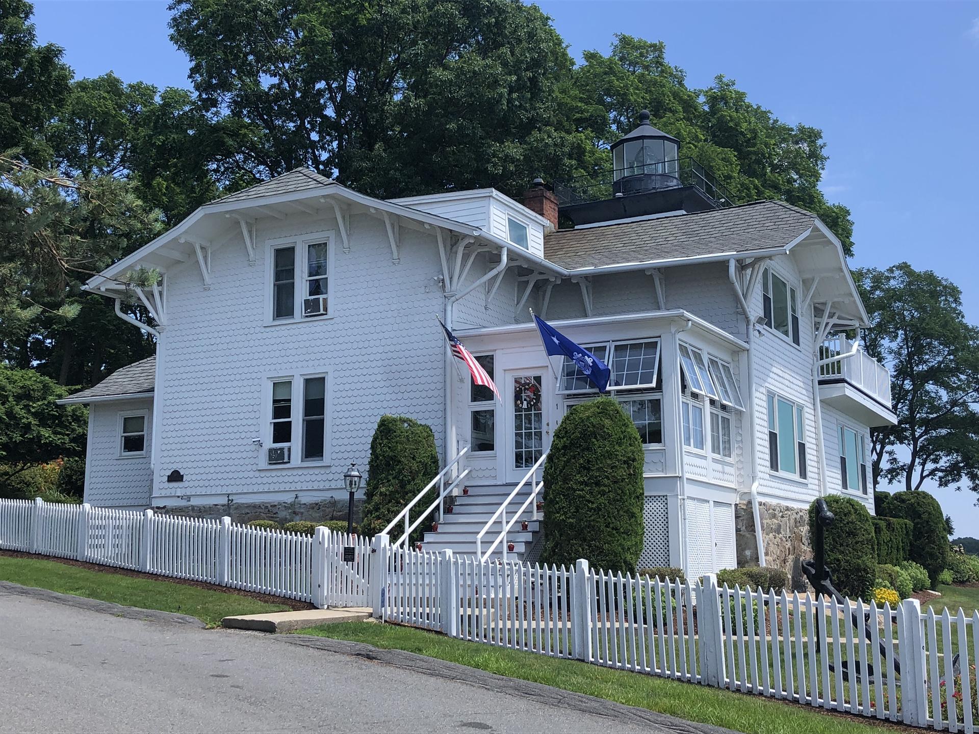 White house with a cupola, picket fence, and flags under a blue sky.