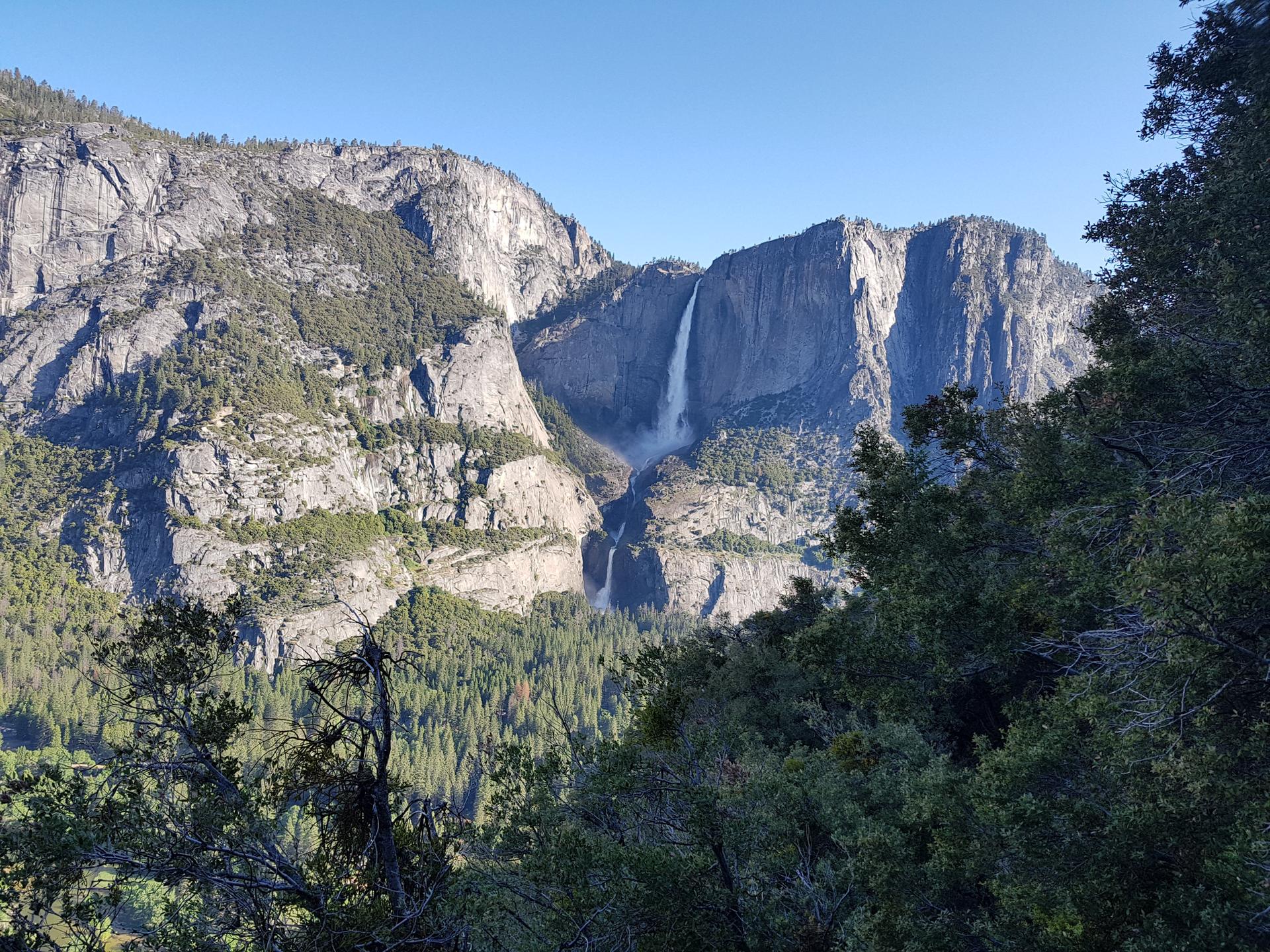Tall waterfall cascading down massive granite cliffs into a green valley.