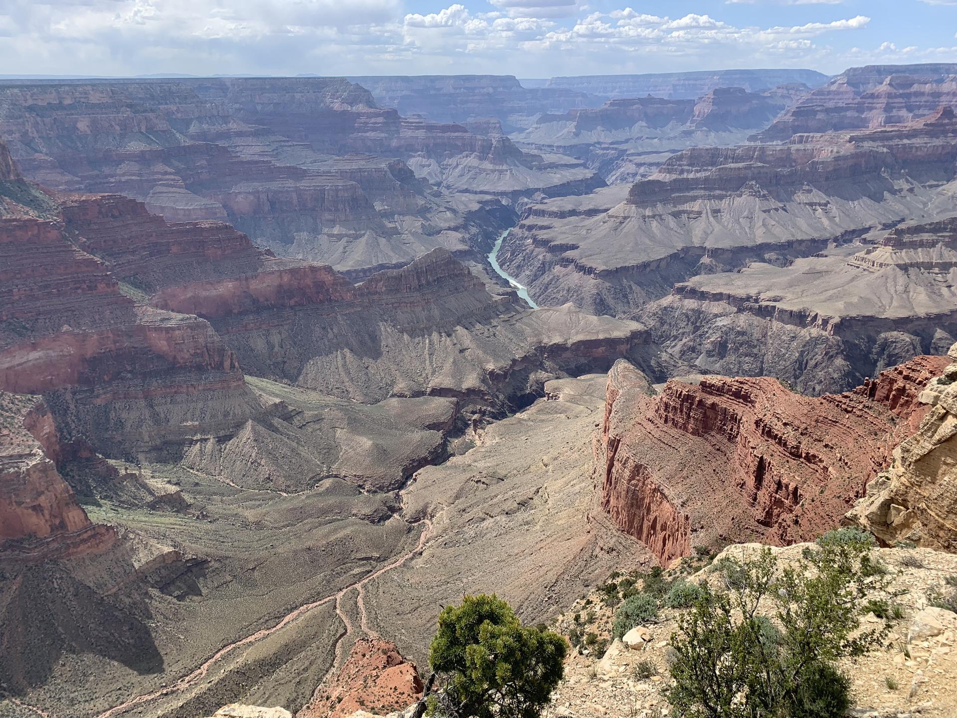 Expansive canyon with a winding river, under a bright, cloudy sky.