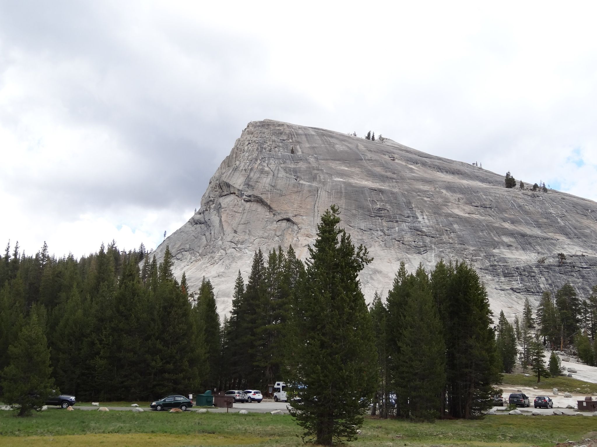 Large granite dome overlooks a pine forest and parking lot under cloudy skies. - Toulumne Meadows to Hetch Hetchy Reservoir