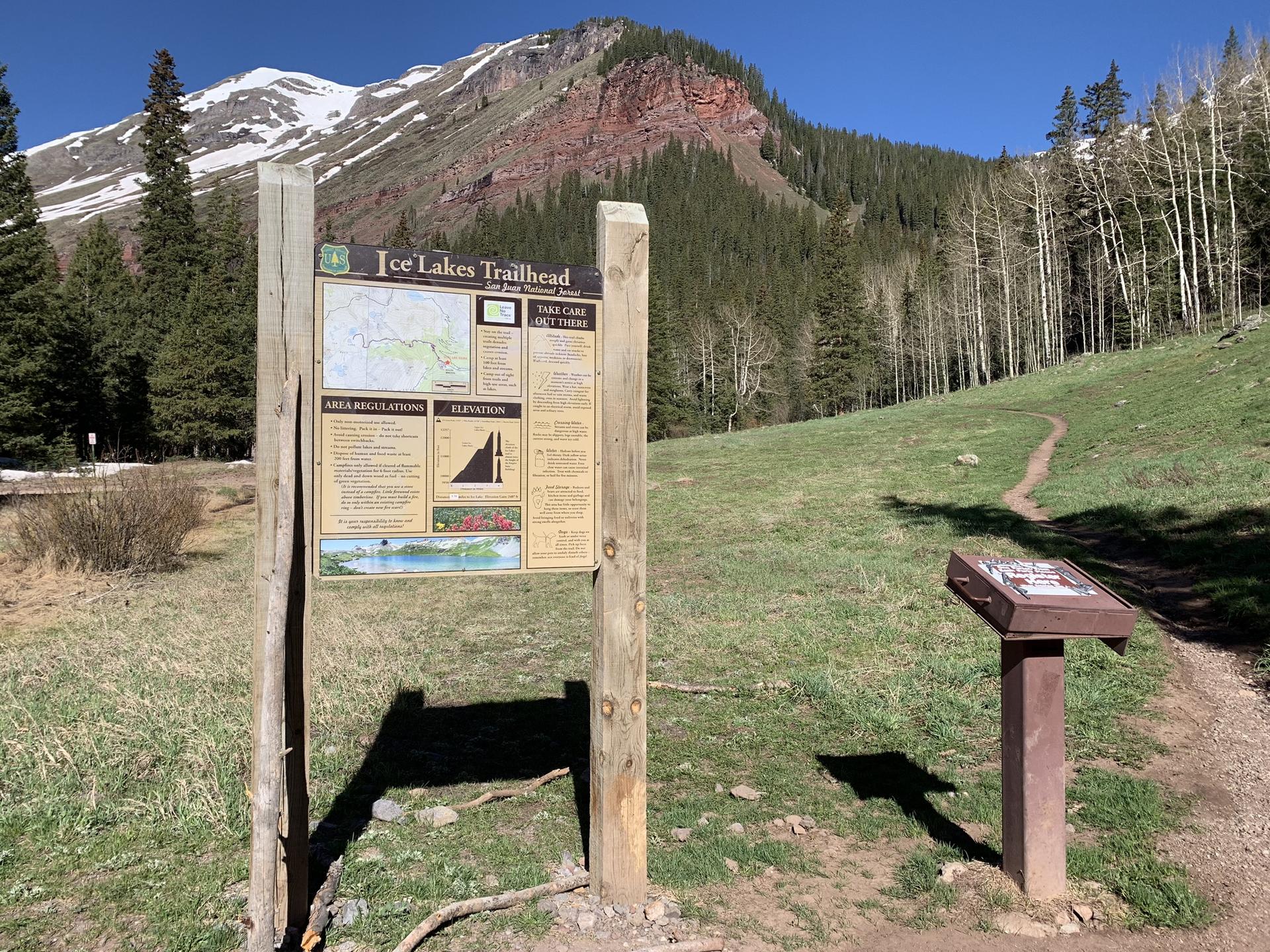 Wooden trailhead sign in a grassy field with a mountain backdrop.