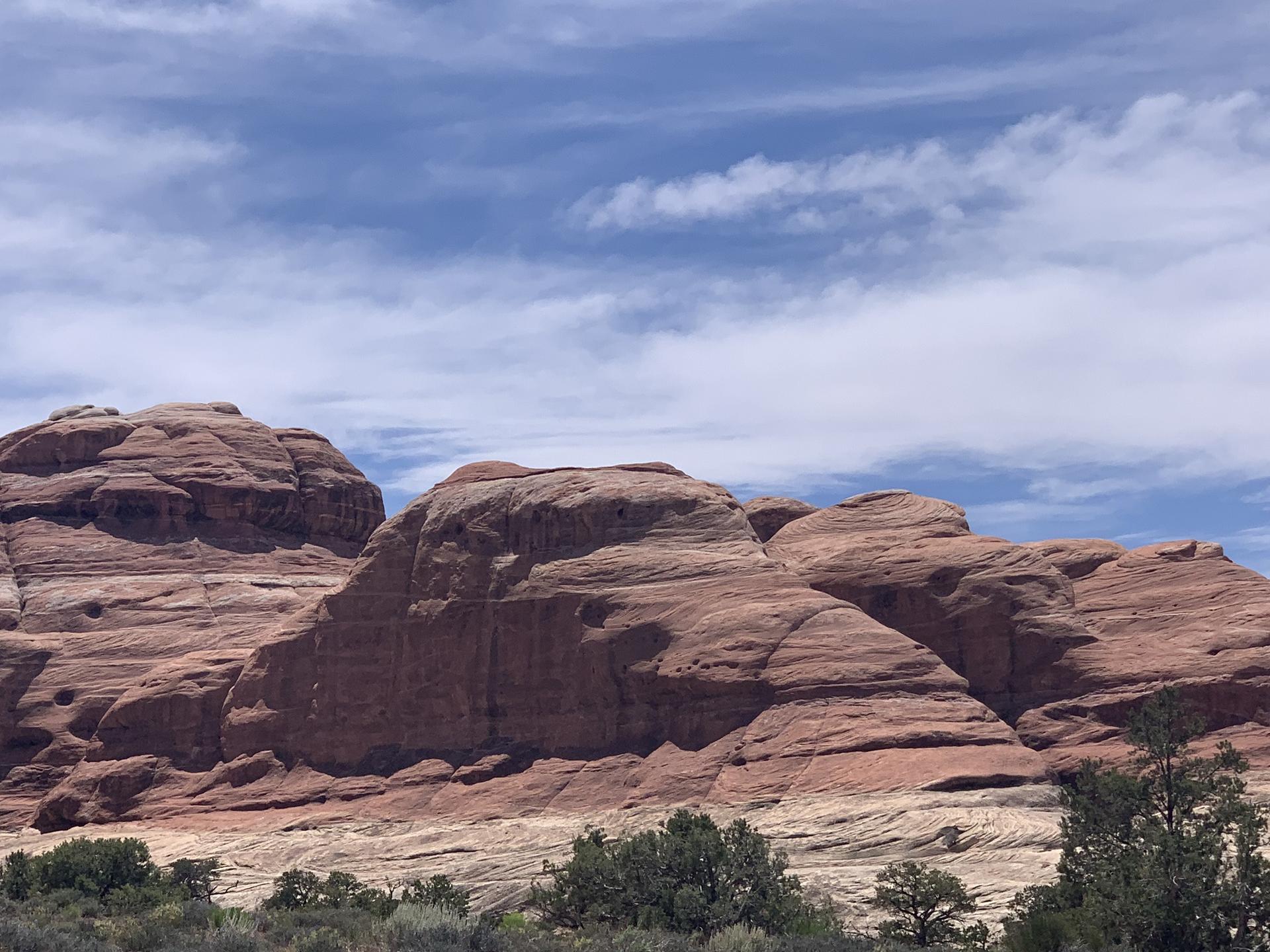 Massive layered red rock formations dominate the desert landscape under blue sky.