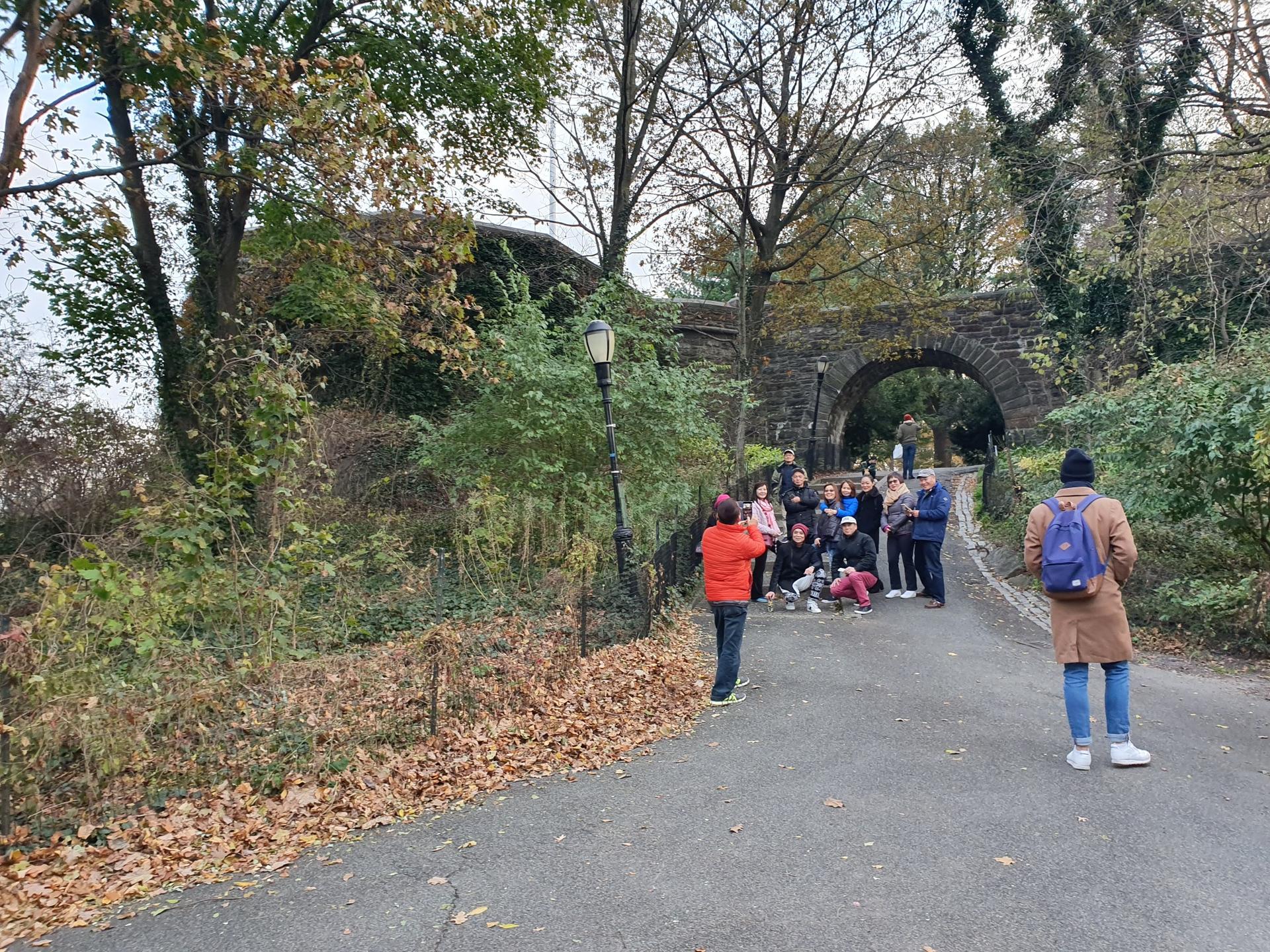 Group of people gathered on a paved path near a stone archway.