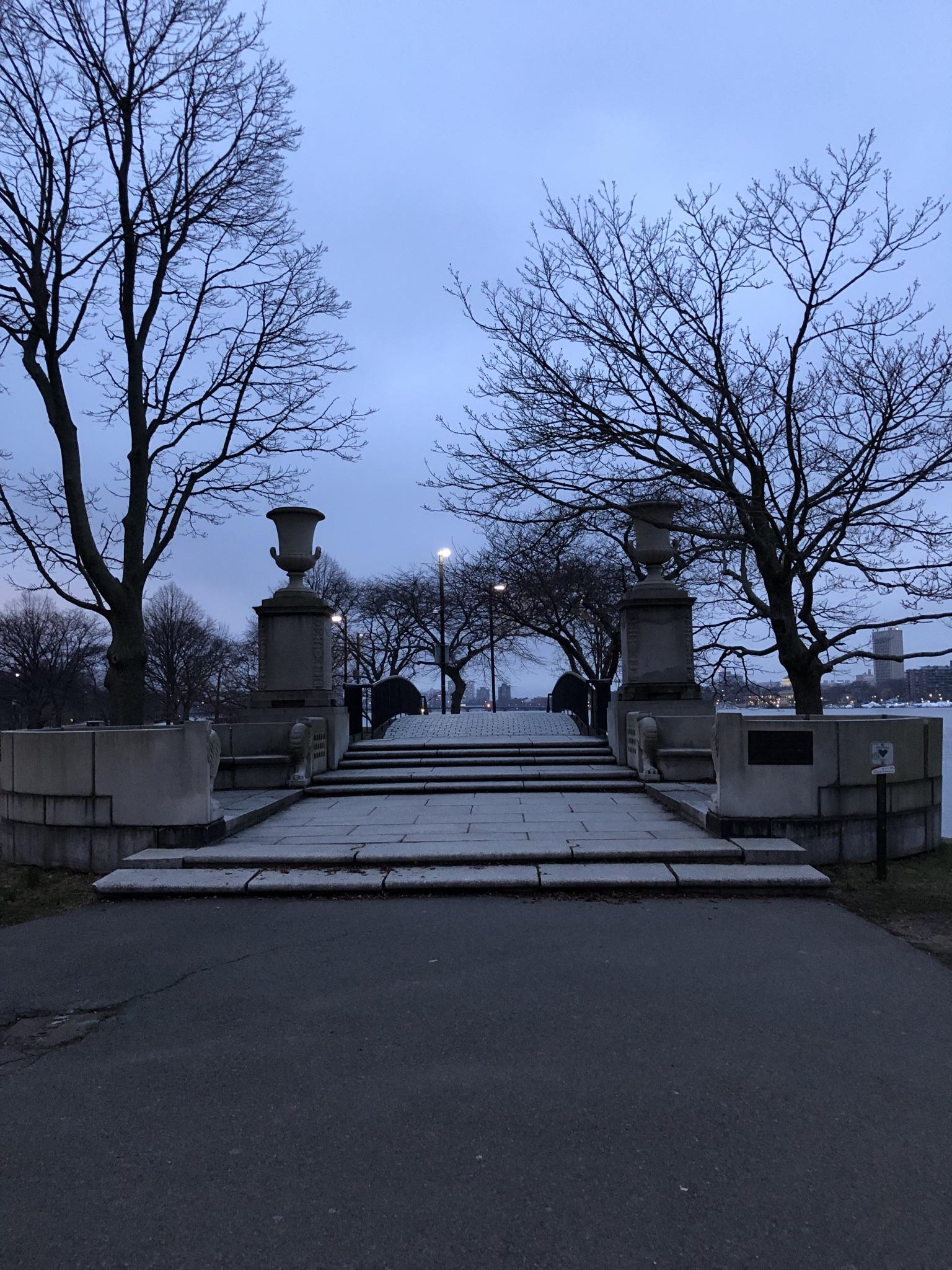 A grand stone staircase with urns leads up, framed by bare trees under a cloudy dusk sky.