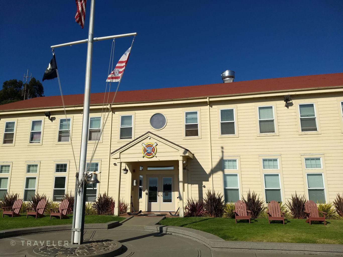 Yellow building with a red roof, flagpole, and Adirondack chairs under bright sun.