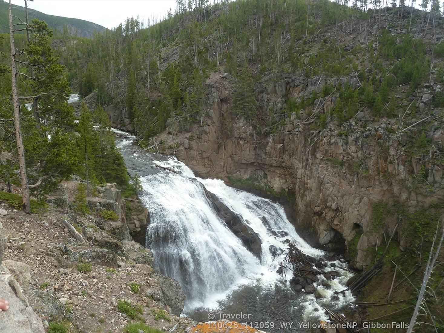 A wide, cascading waterfall flows over rocks amidst green, forested slopes.