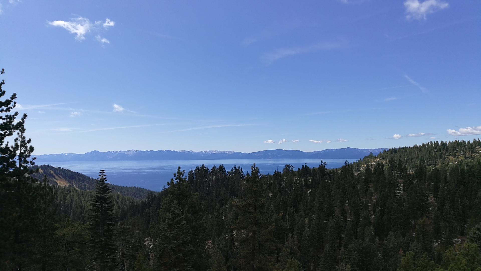 Wide view of a large blue lake framed by dense green forests and mountains.