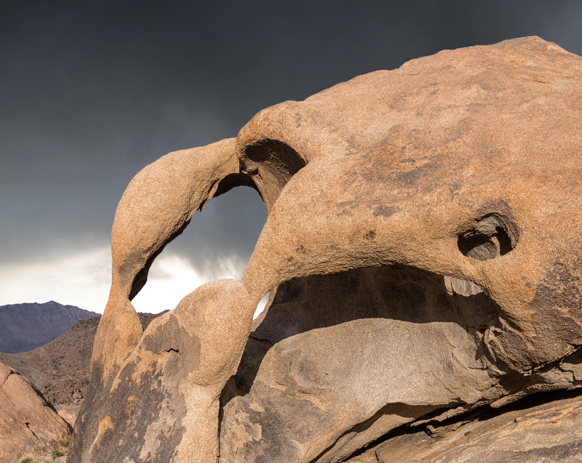 Intricate rock formation with a natural arch under a dramatic, dark sky.