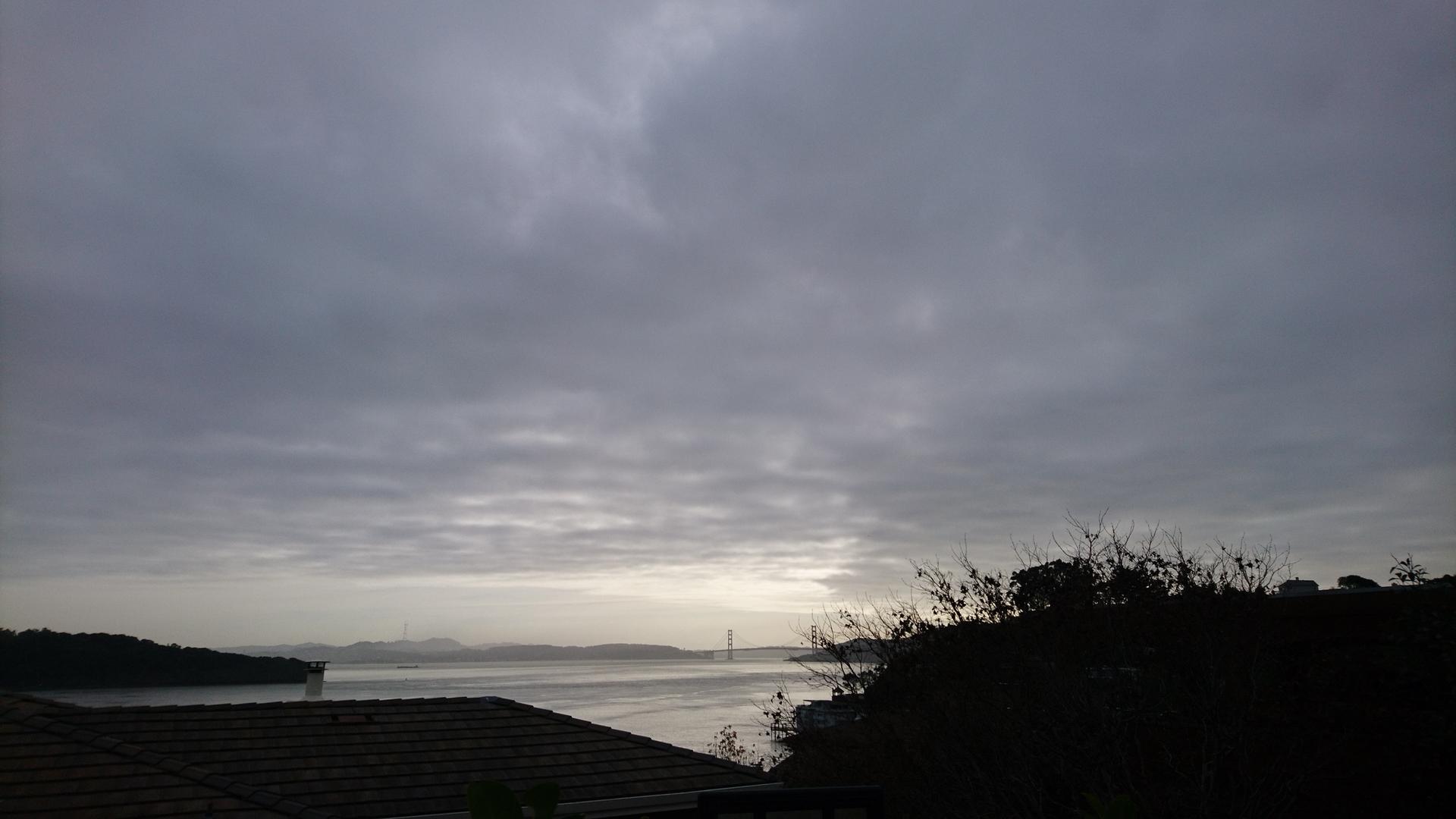 Dark, cloudy sky over water and distant land, with muted light.
