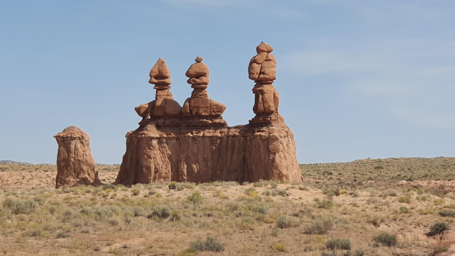 Three distinct, stacked rock formations rise from a sparse desert landscape.