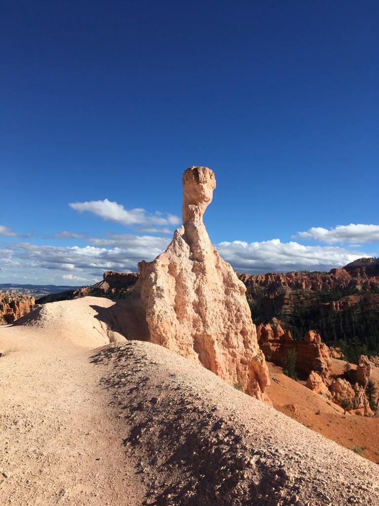 Unique light orange rock formation resembling a figure under a clear blue sky.
