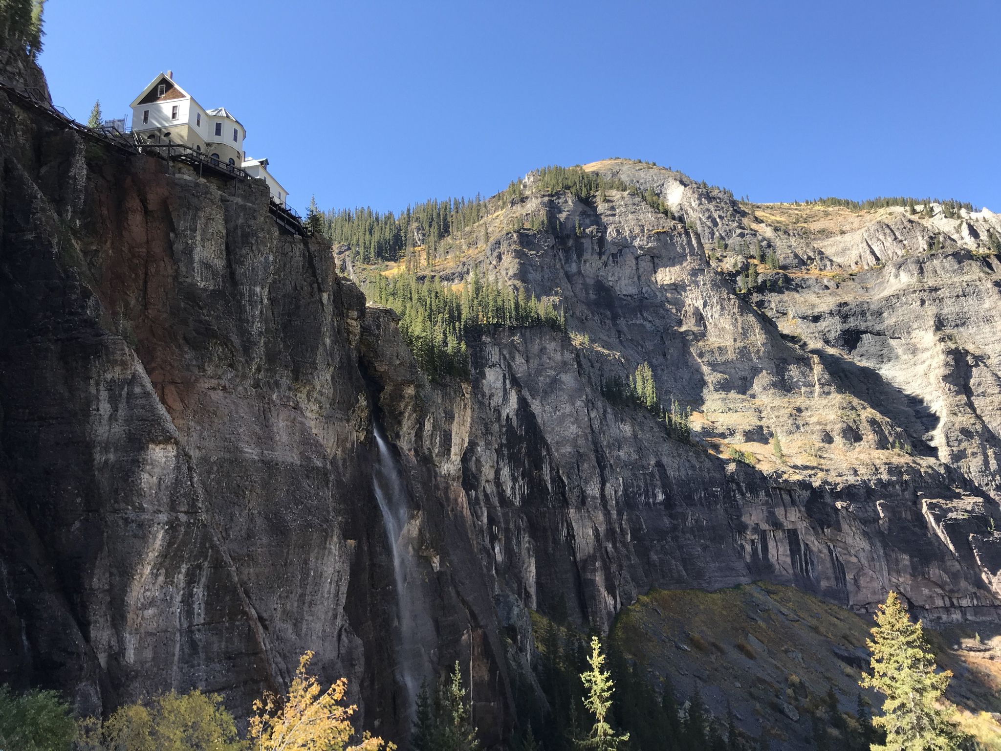 White building perched on a cliff beside a waterfall under a clear sky. - Bridal Veil Falls, Black Bear Pass Loop
