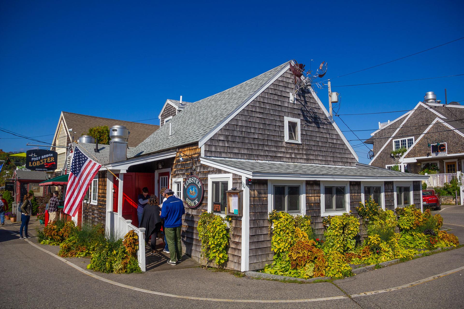 Shingled building with an American flag, people entering, under clear blue sky.