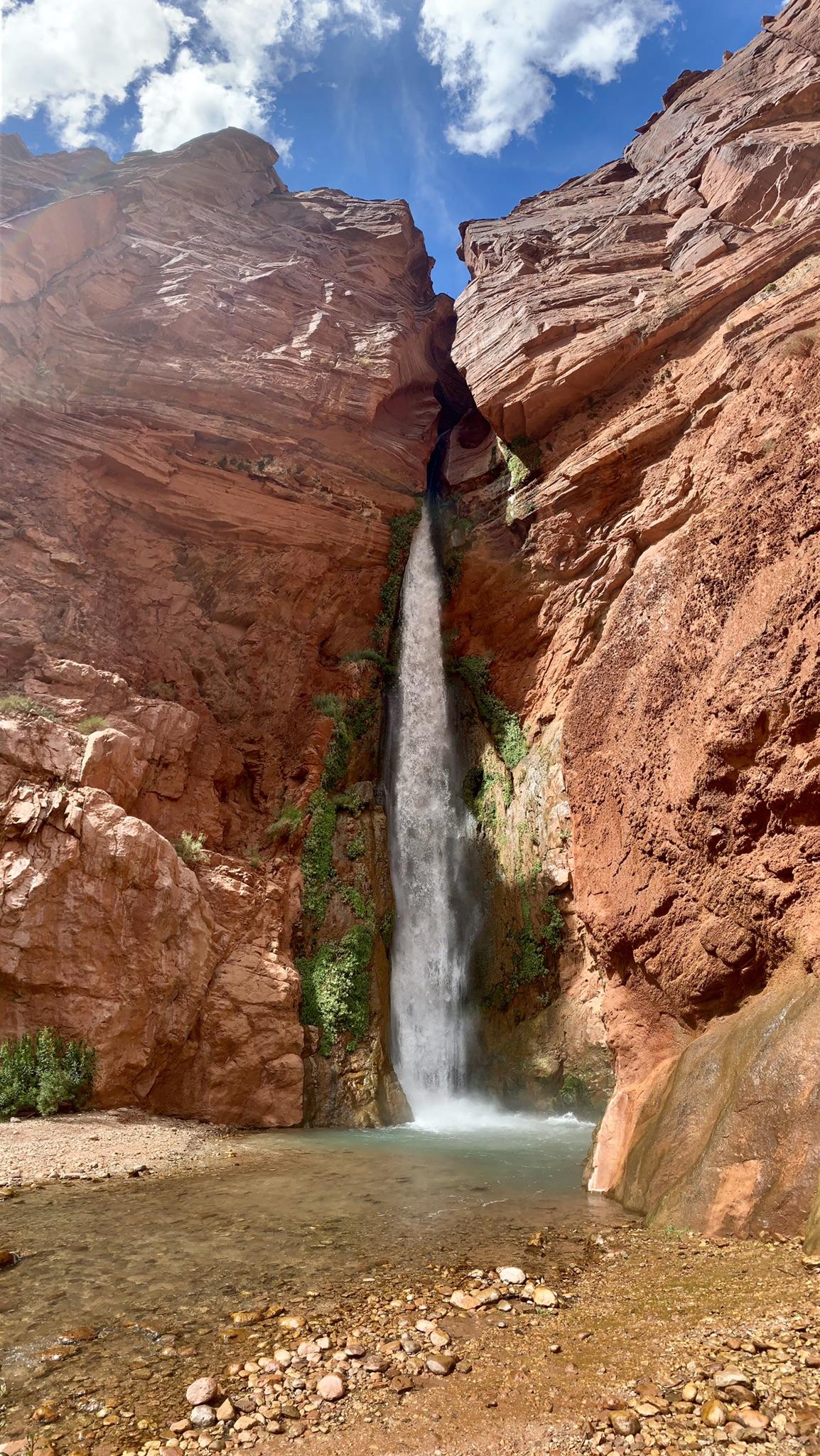Tall waterfall cascading into a clear pool between towering red canyon walls.