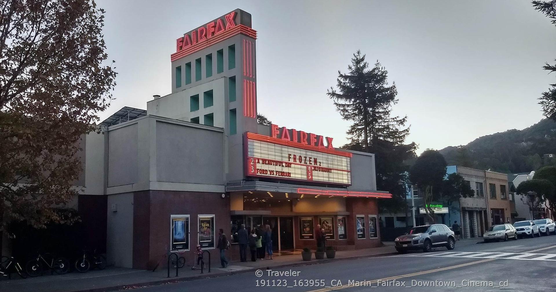 Art deco theater with neon sign, people entering, under cloudy skies.