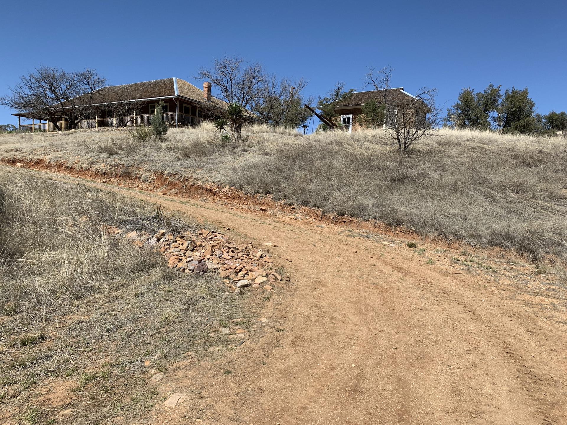 Two old buildings on a dry hill with a dirt road in bright daylight.