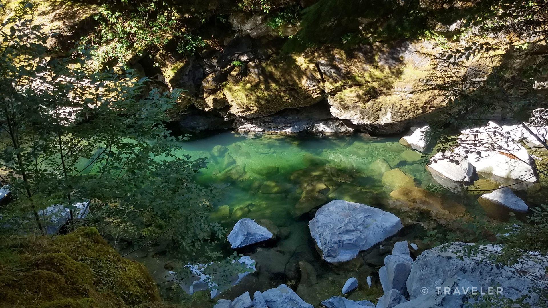 Clear green river flowing through a shaded, rocky gorge with dappled sunlight.