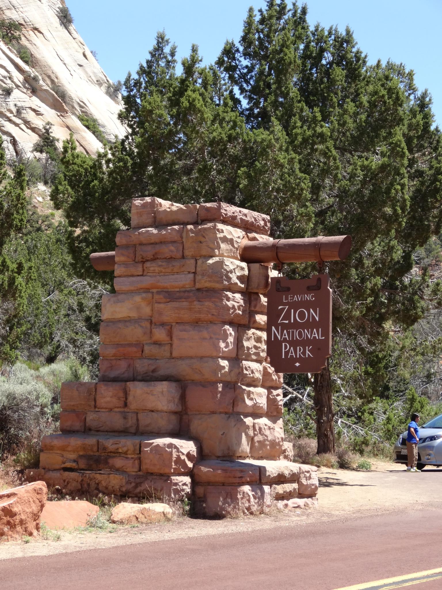 Stone monument with a wooden sign, person, and car on a sunny day.