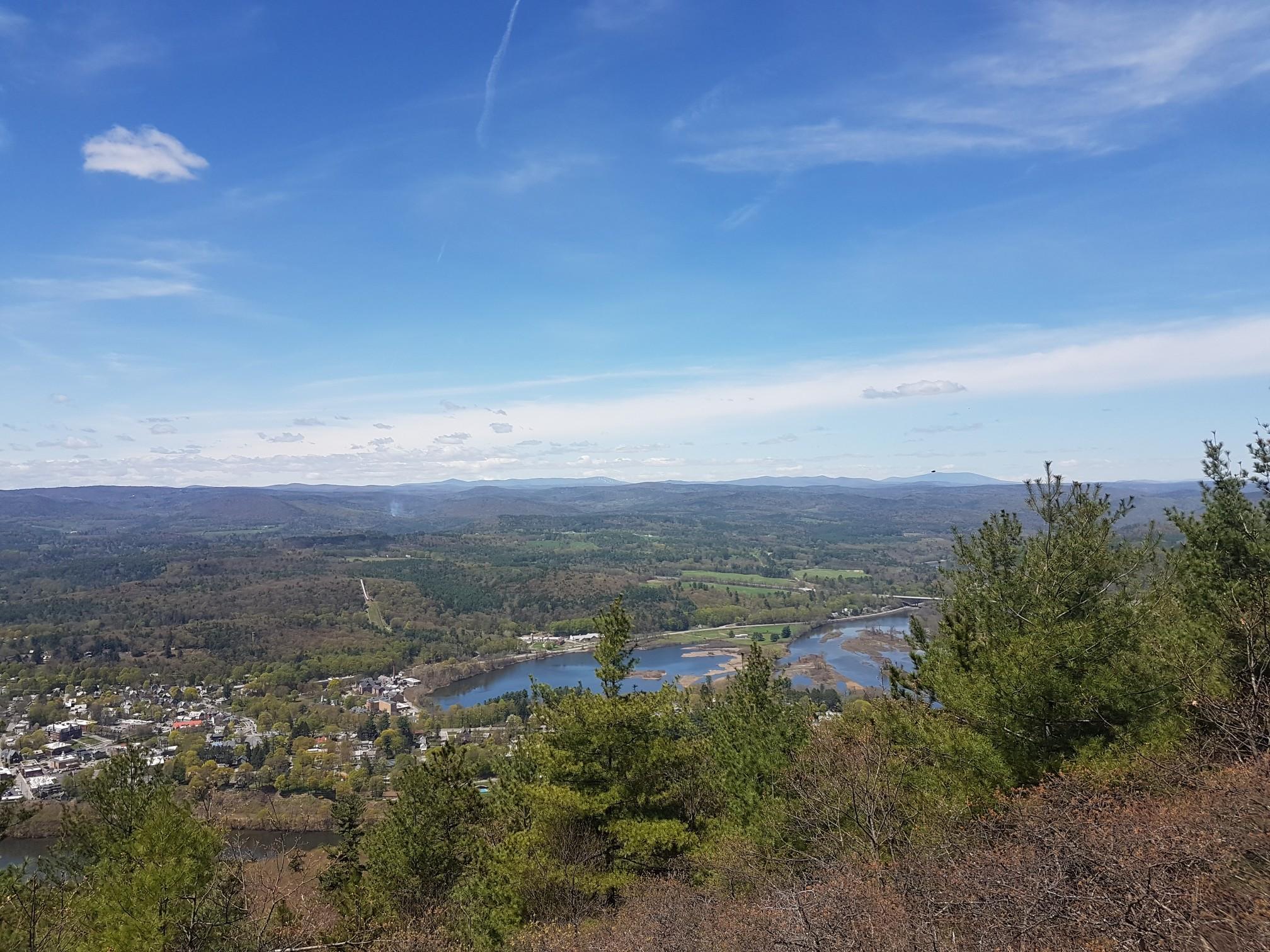 Panoramic view of a river, town, and forested valley under a bright blue sky.