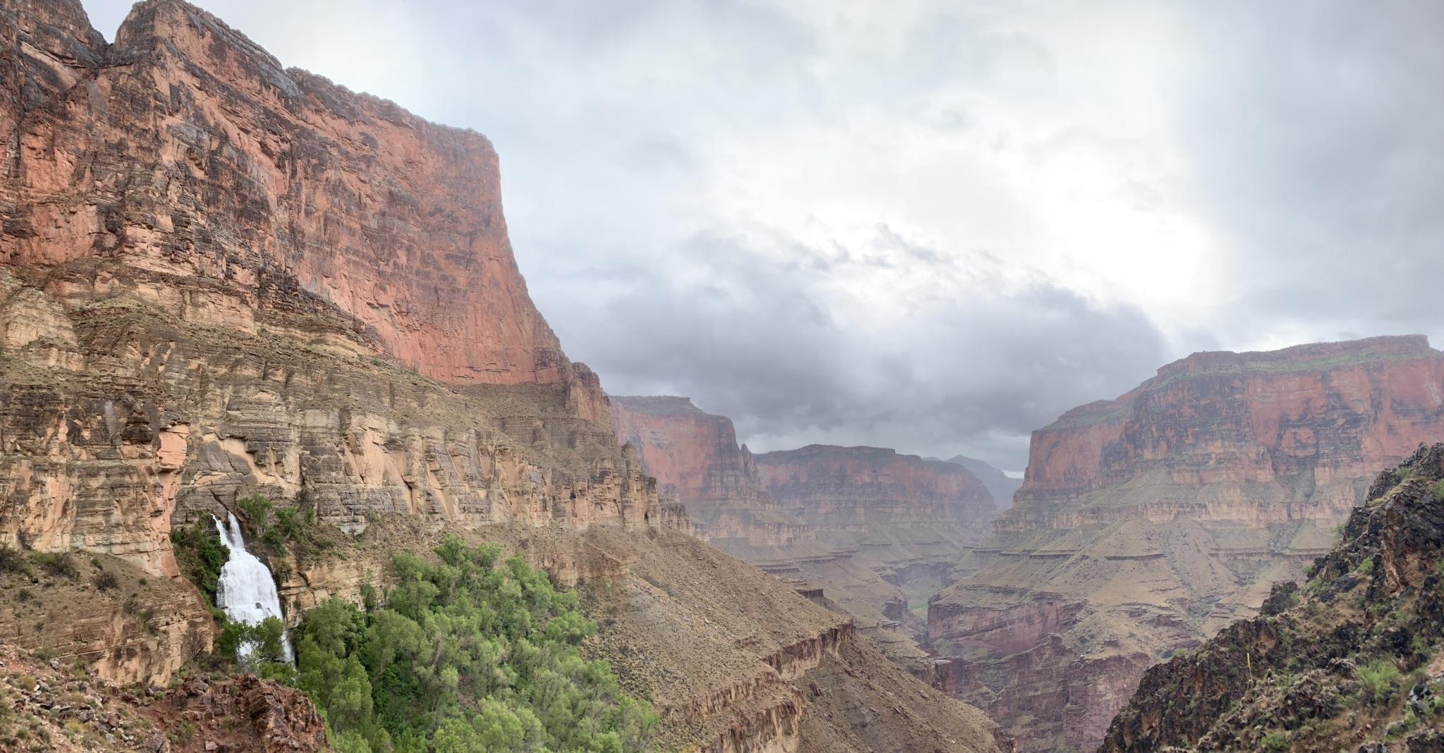 Overcast sky above a deep canyon with a waterfall and green vegetation.
